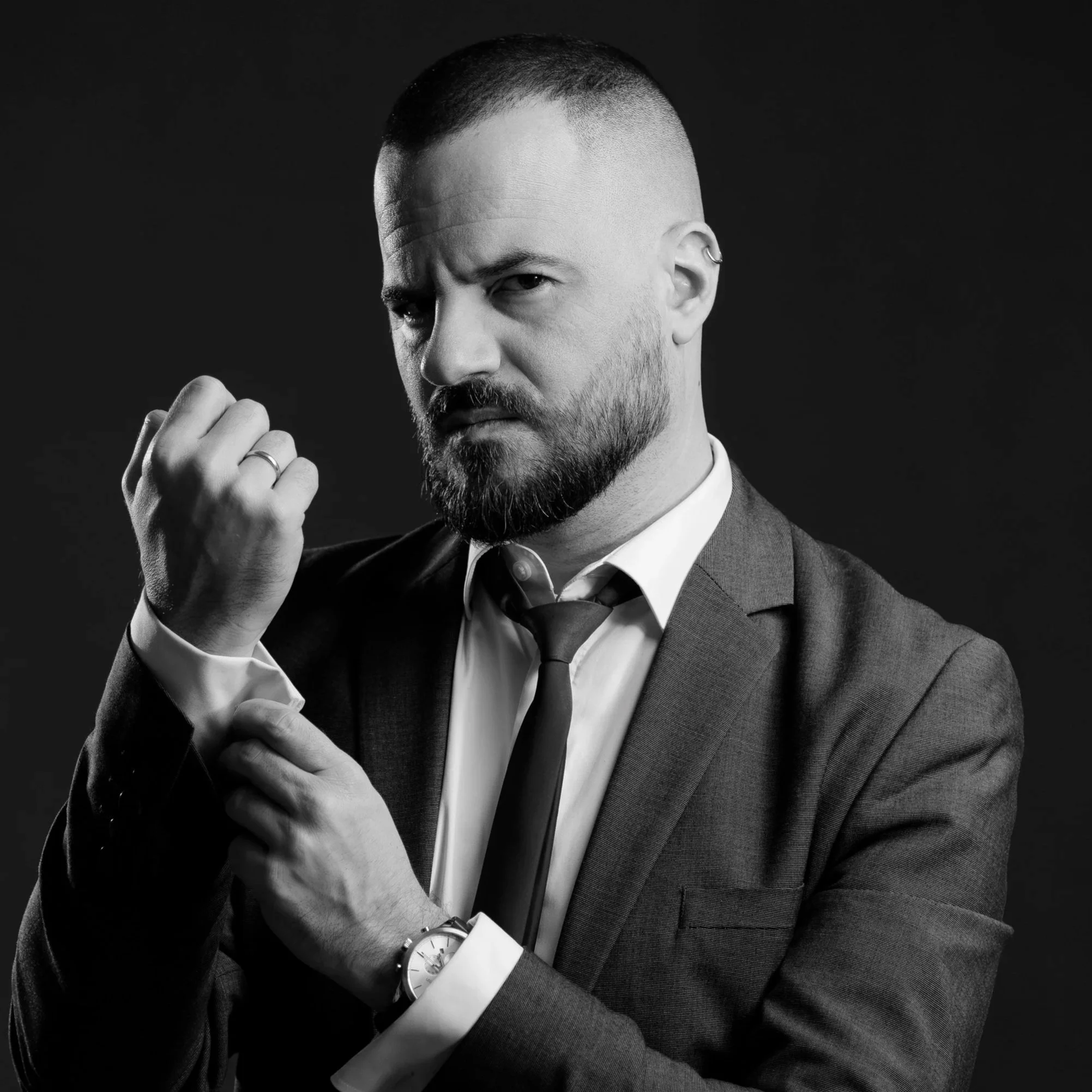 Black and white portrait of a serious man in a suit fixing his cuff and looking at the camera.