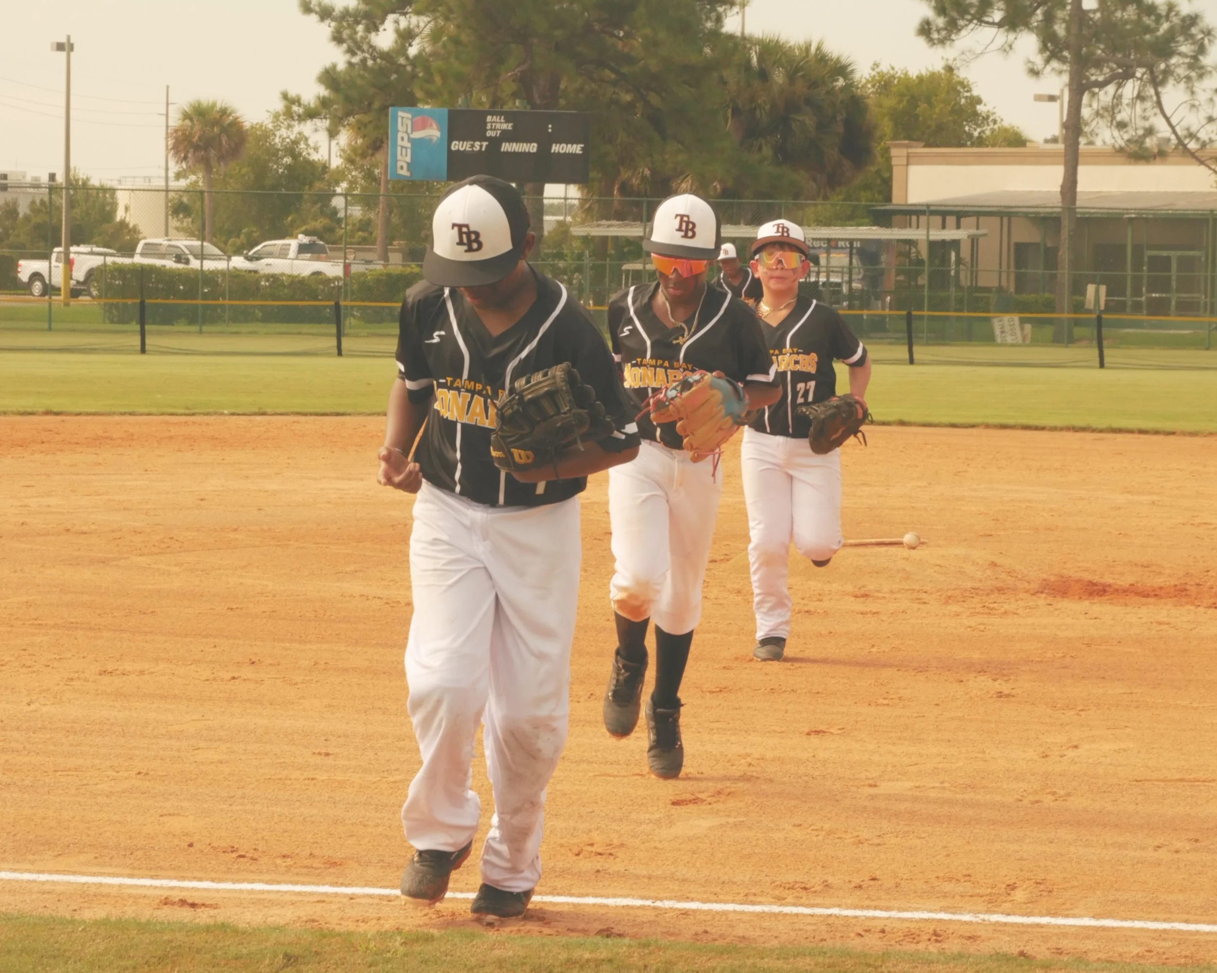 Three baseball players in black and white uniforms jogging on a baseball field during daytime.
