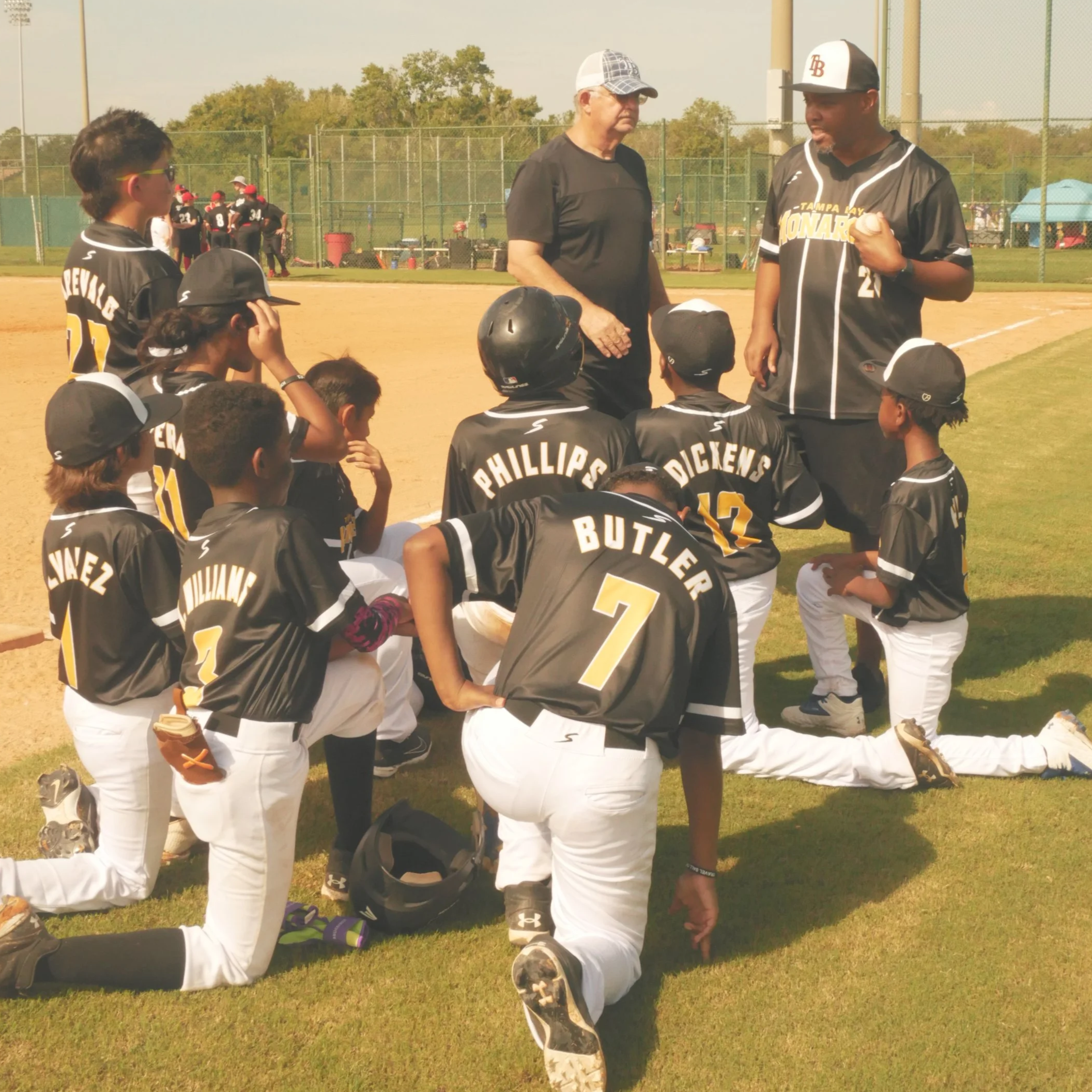 Young baseball players in black uniforms listening to coaches on a baseball field during a game or practice.
