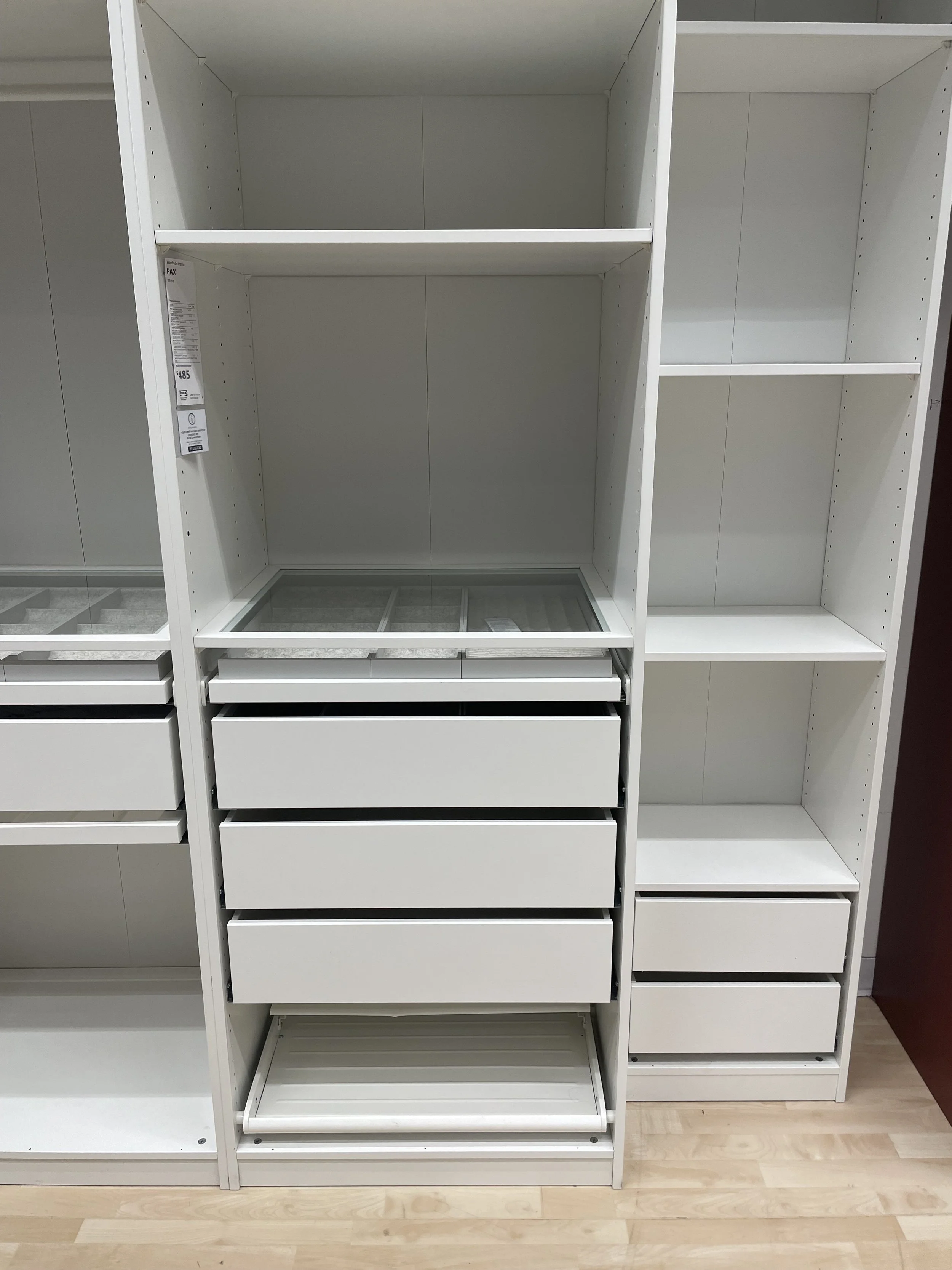 Empty white shelving unit with drawers and glass display area, in a retail store.