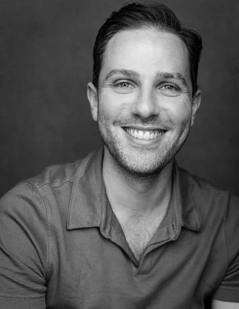 Black and white portrait of a smiling man with short hair, wearing a collared shirt.