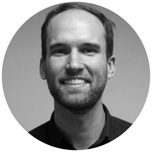 Black and white portrait of a smiling man with short hair and a beard, wearing a dark collared shirt, against a plain background.
