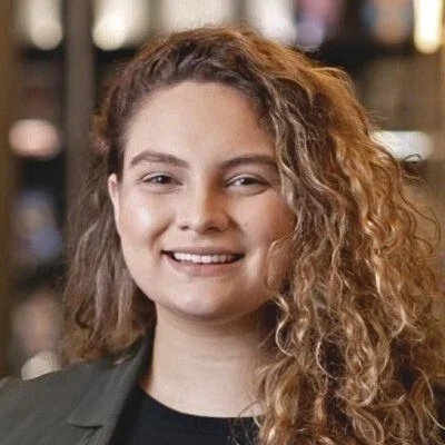 A woman with curly hair smiling at the camera indoors.
