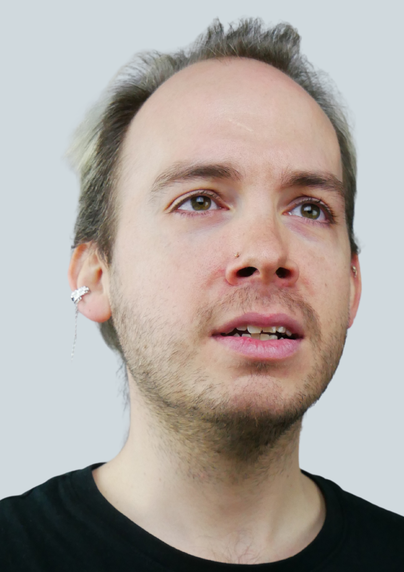 Close-up of a young man with light skin and short, light brown hair with gray tint, wearing earrings, a nose piercing, and a black shirt, looking slightly to the right against a plain light background.