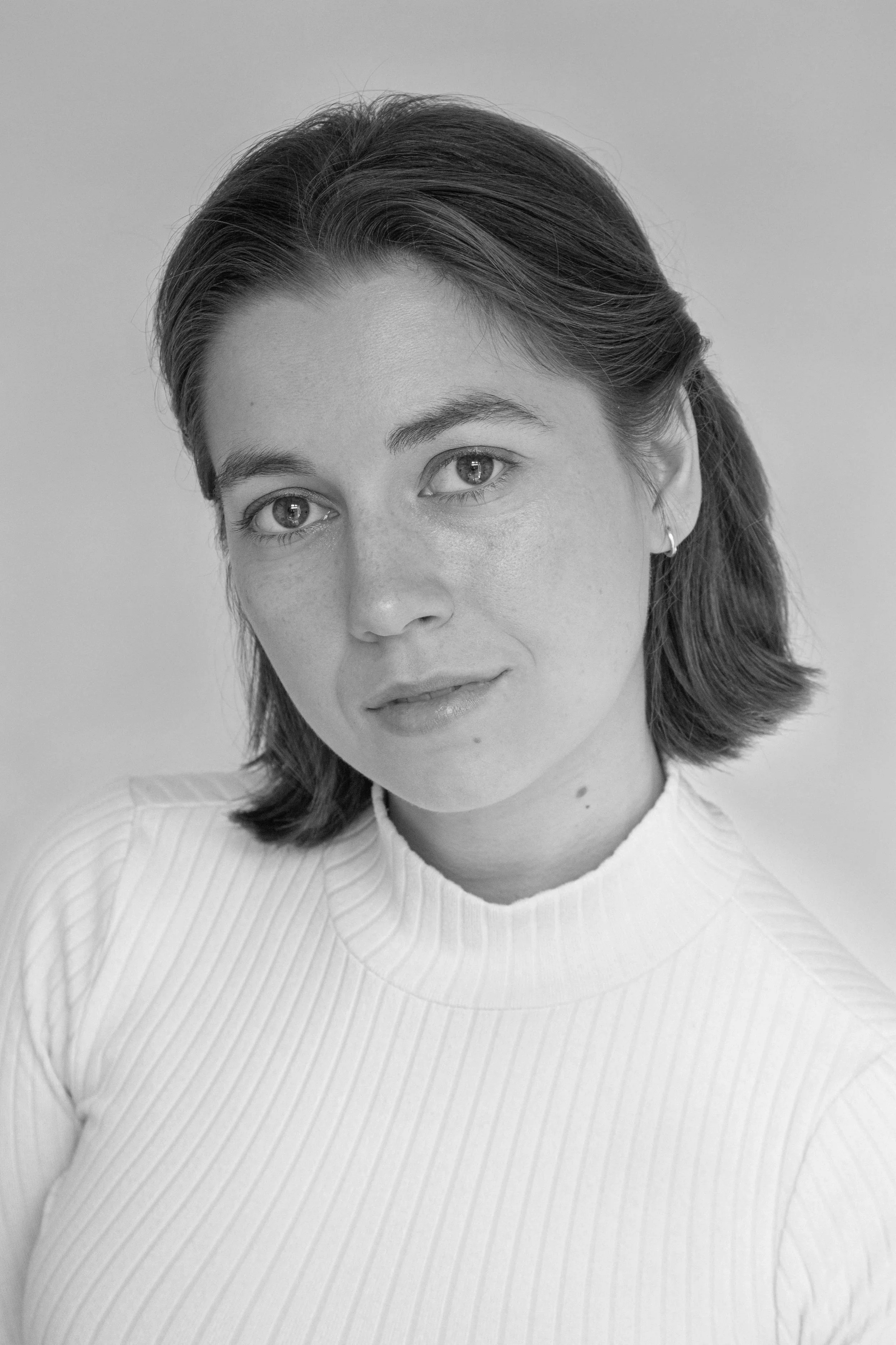 Black and white portrait of a young woman with short, wavy hair, wearing a ribbed turtleneck top, looking slightly to the side.