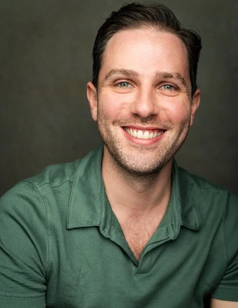 Close-up of a smiling man with dark hair, wearing a green collared shirt, against a gray background.