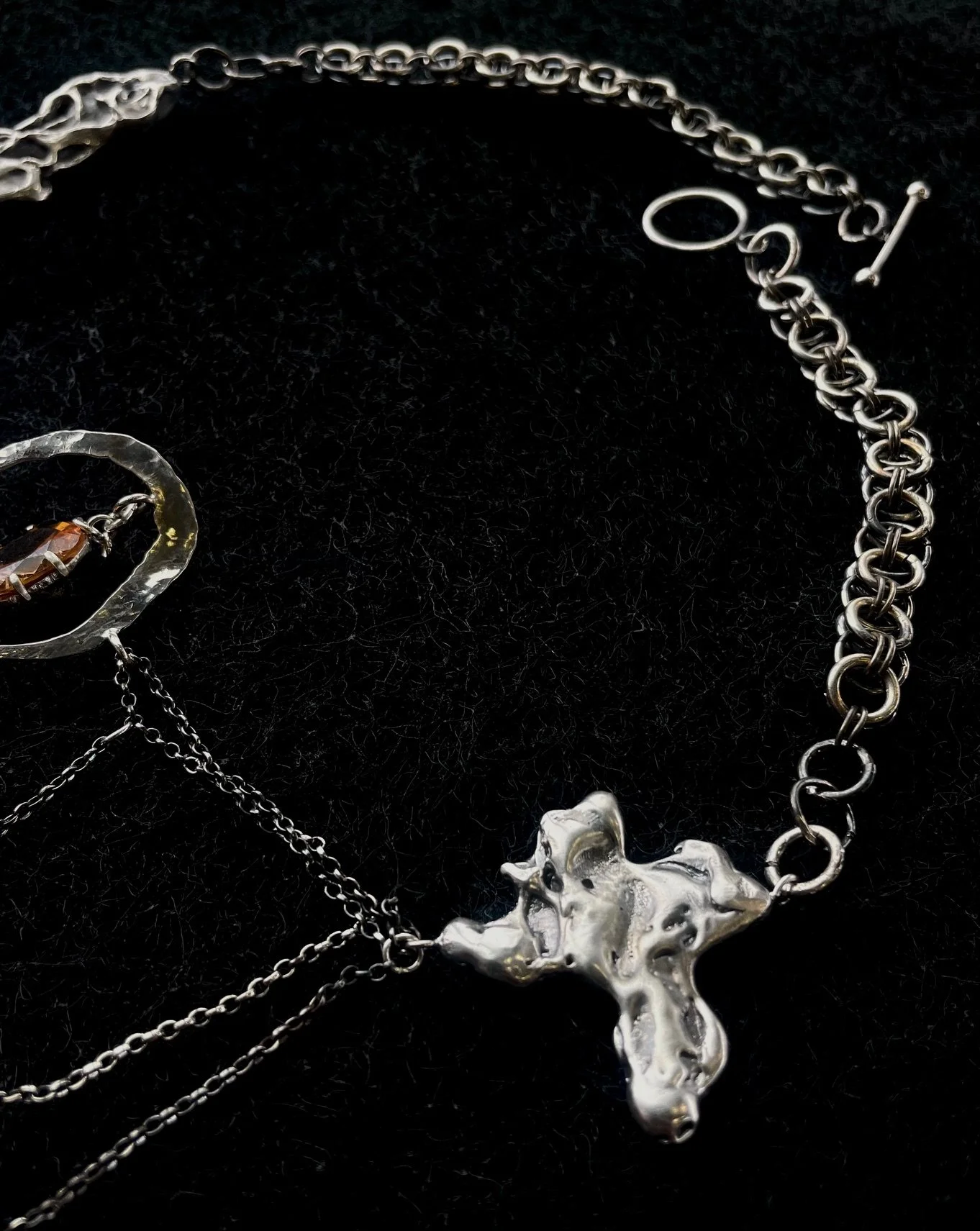 Silver cross necklace with a chain, alongside a silver chain and a small charm, displayed on a black background.