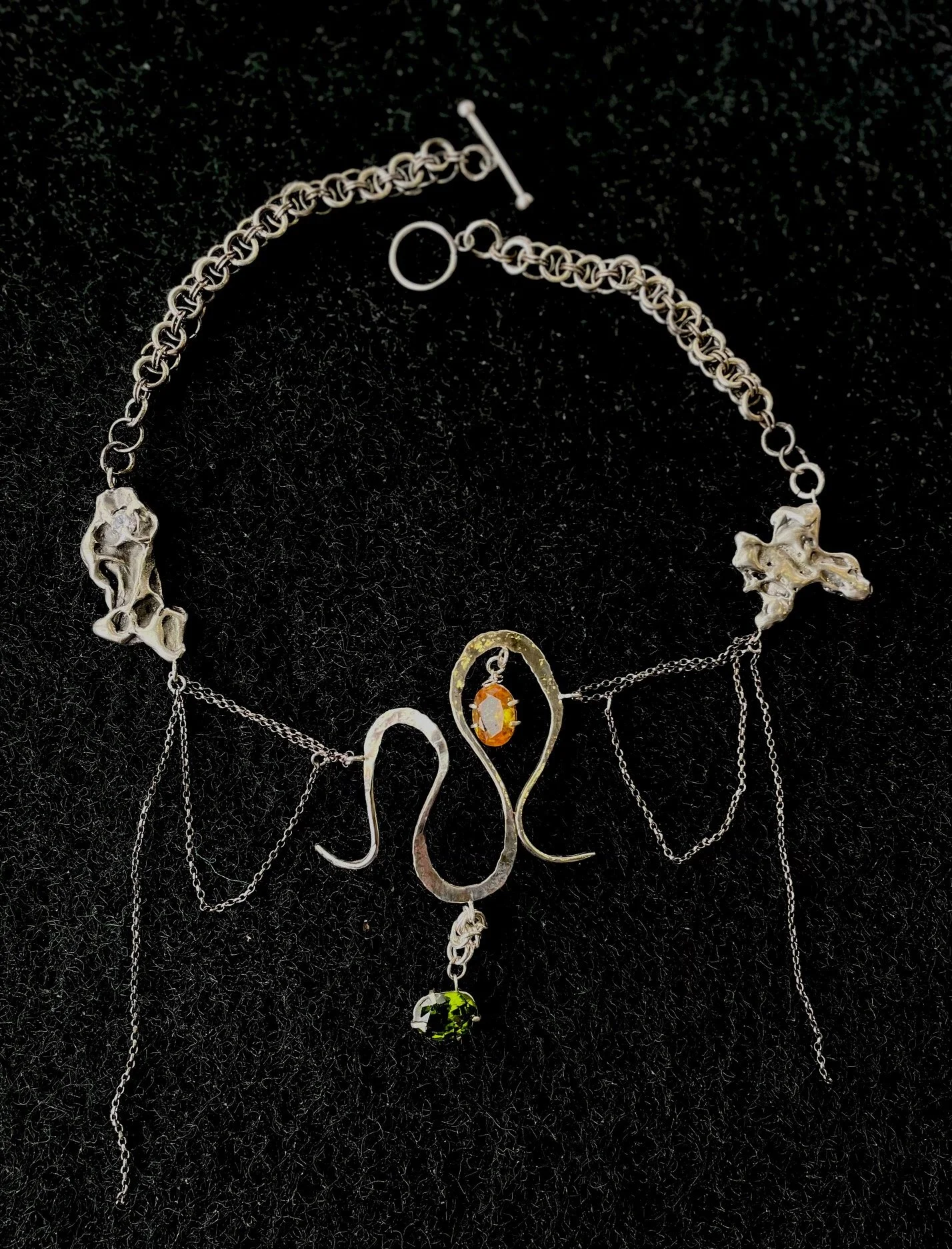 Sterling silver necklace with chainmaille and dramatic silver embellishments on each side. Swirling centerpiece with hanging orange and green stones and dainty dangling chain