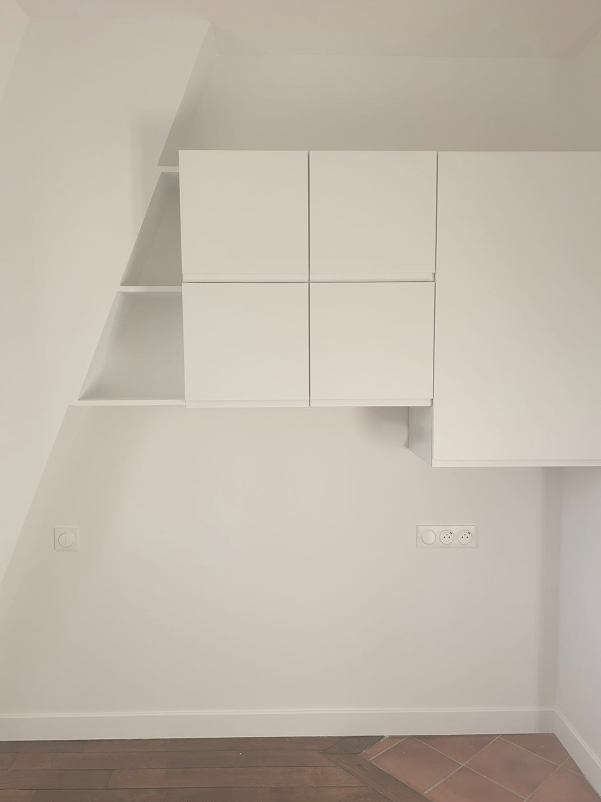 Une installation murale blanche avec des compartiments de rangement et des étagères dans une pièce, avec des prises électriques visibles.