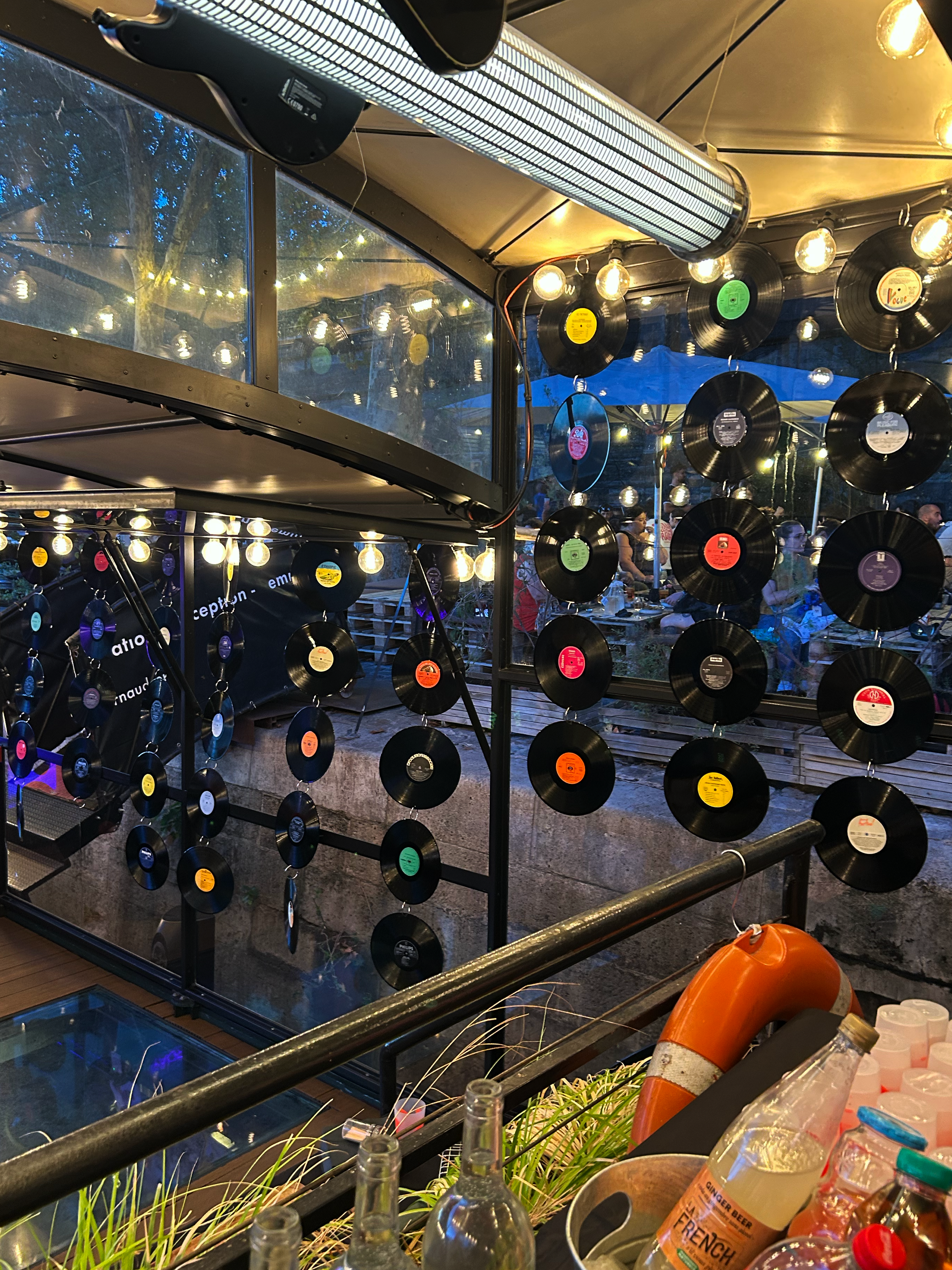 Décoration intérieure d’un bar avec de nombreux vinyles suspendus, ampoules vintage et grandes fenêtres donnant sur l’extérieur.