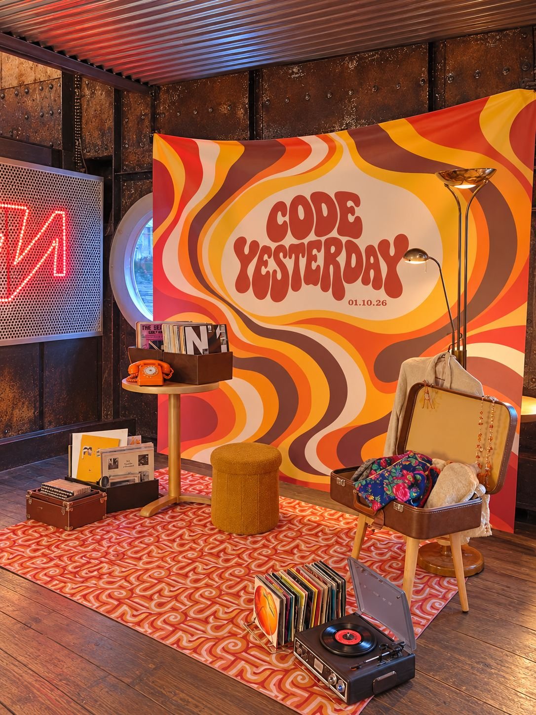 Décor rétro coloré « Code Yesterday » avec platine vinyle, disques, téléphone orange, valises vintage et fauteuil.