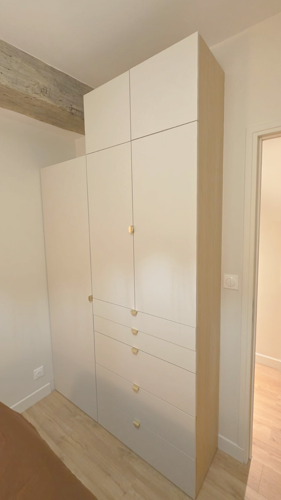 Grand meuble de rangement blanc avec plusieurs portes et tiroirs en pin clair dans une pièce.