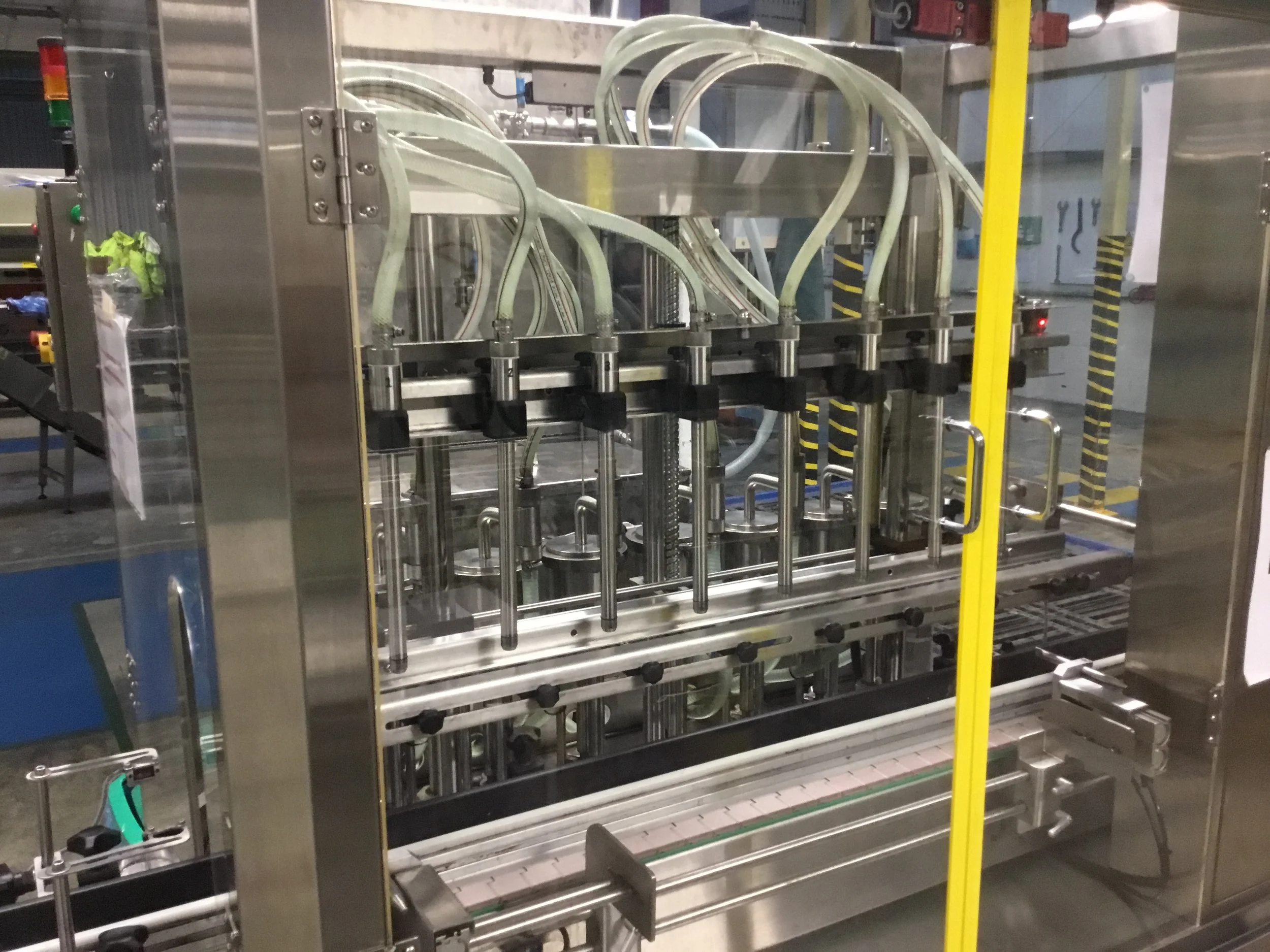 Stainless steel industrial filling or capping machine with multiple nozzles and tubes in a manufacturing facility.