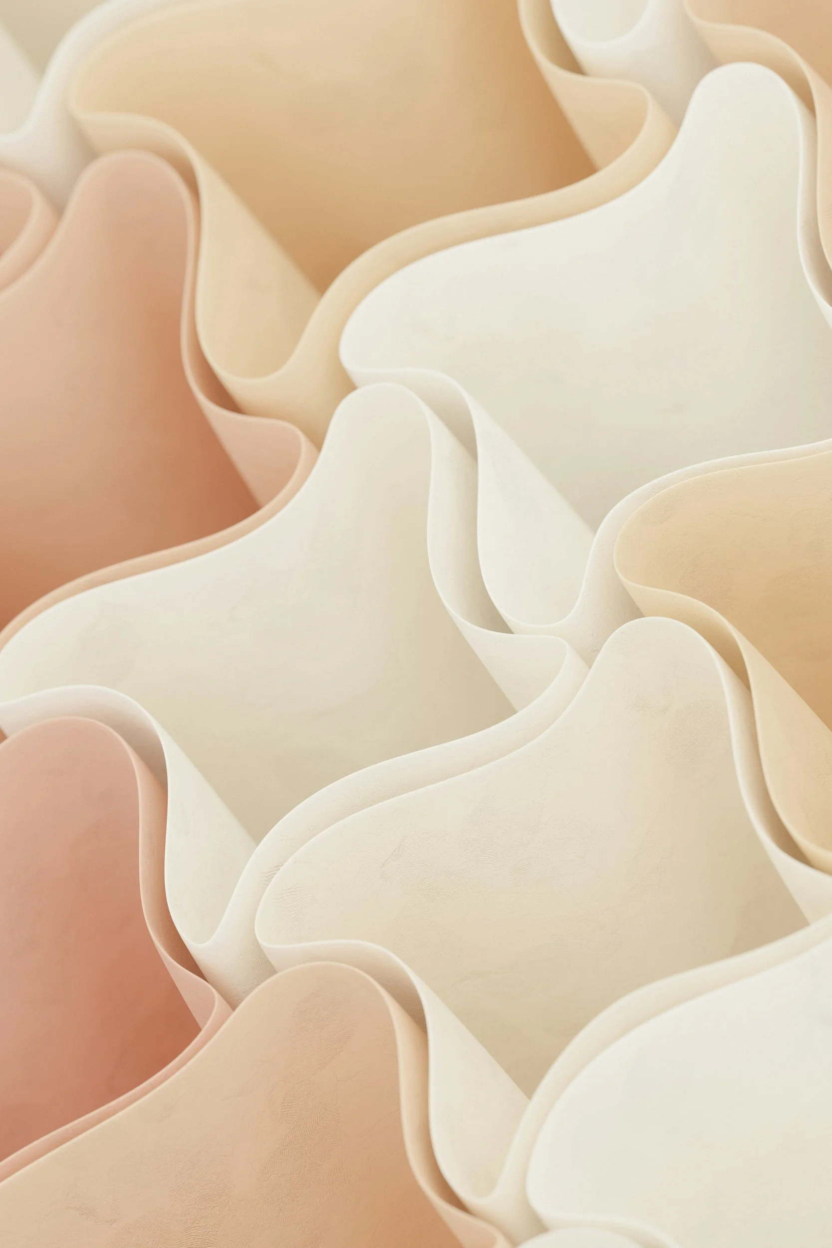 Close-up of layered, wavy, pastel-colored paper or fabric materials creating a textured, abstract pattern.