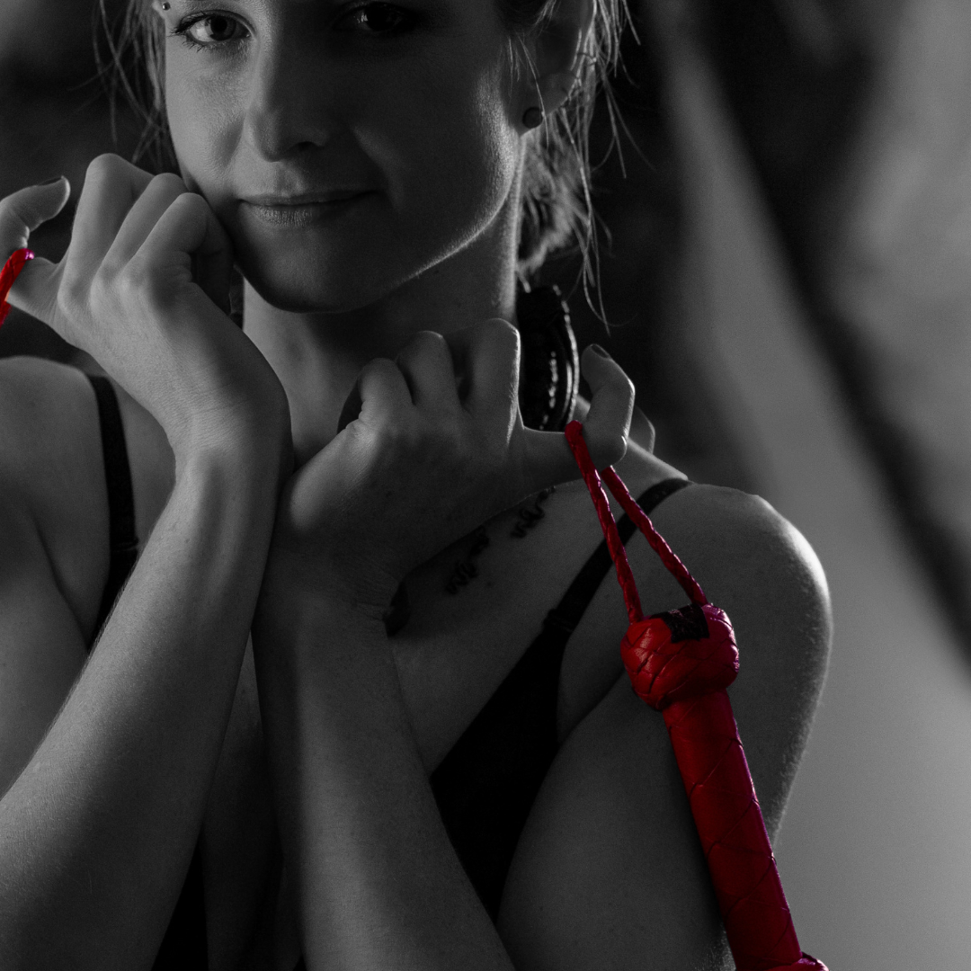 A black and white portrait of a woman with a serious expression, holding a red boxing glove and hand wraps, with some red color added to the gloves and wraps.