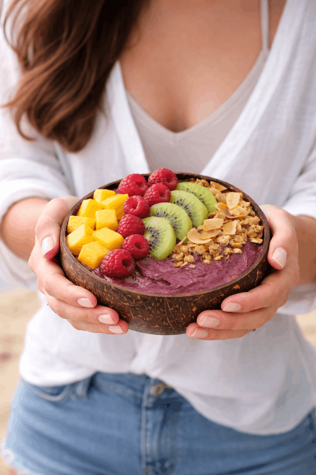 Persona sosteniendo un tazón con yogur, mango, frambuesas, kiwi y avena.