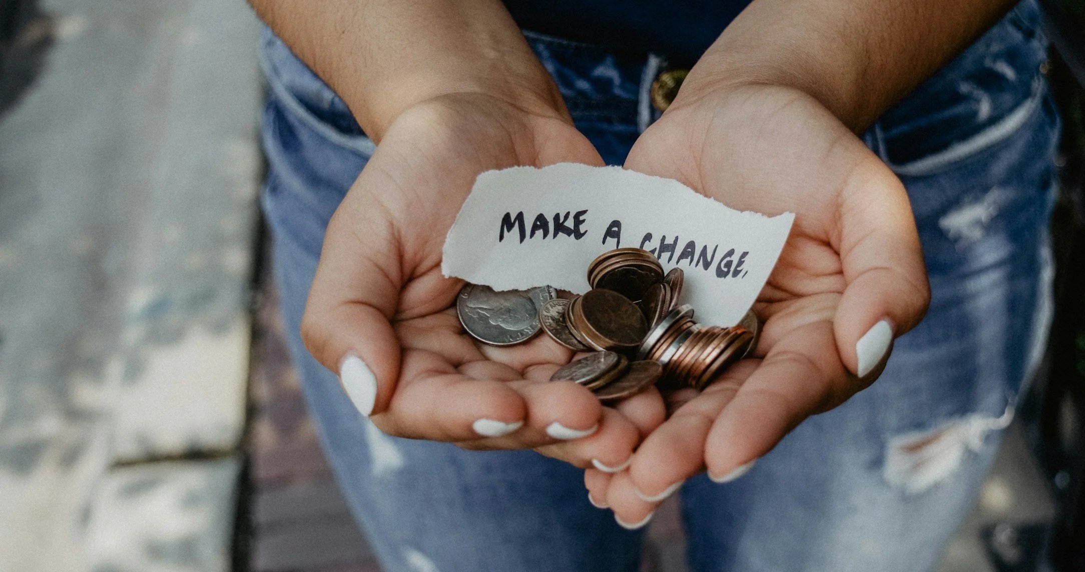 Manos sosteniendo monedas con una nota que dice Make a change, símbolo de la donación a los proyectos socioeducativos de la Fundación Ángel Linares