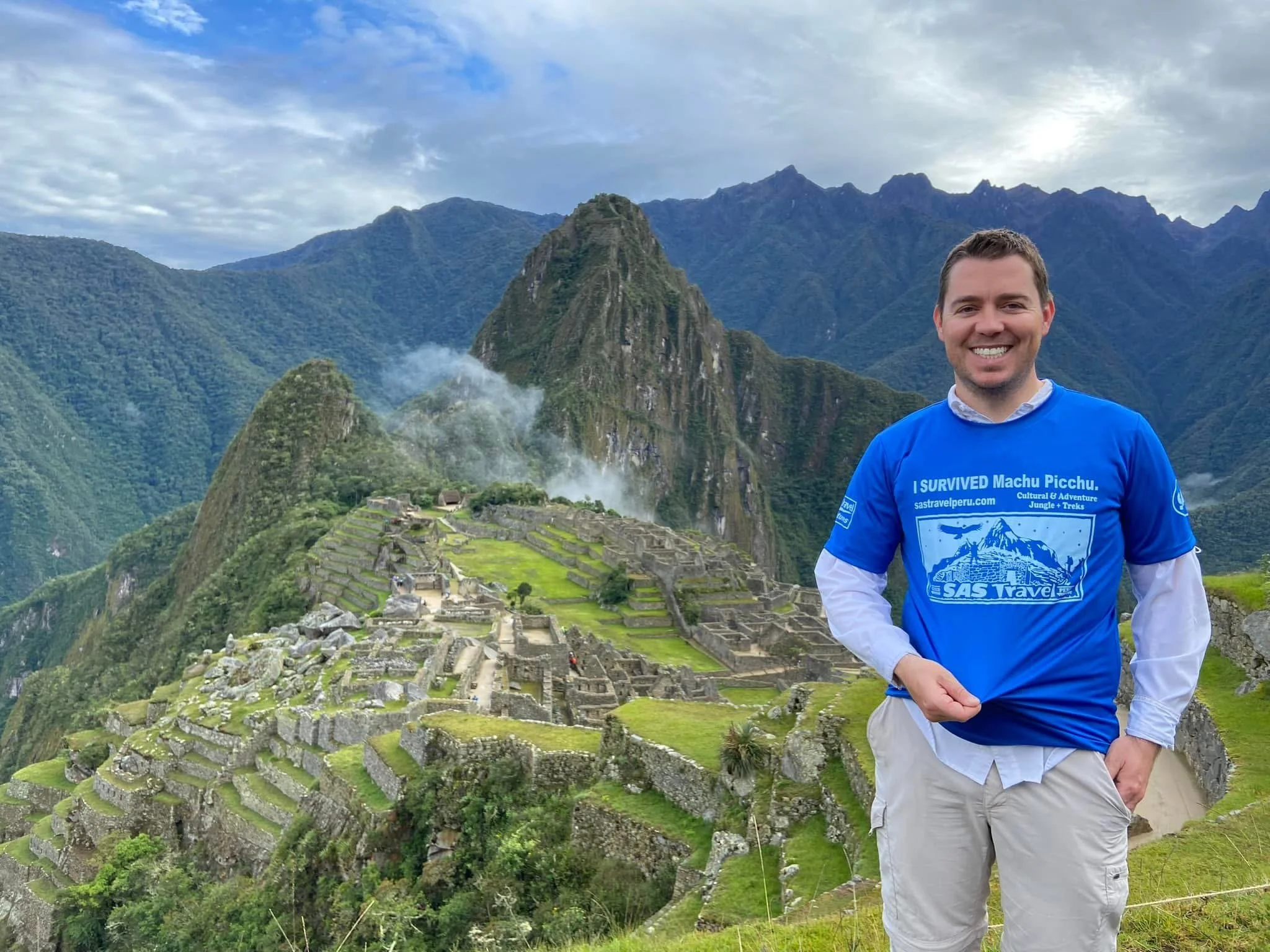 Man smiling in front of Machu Picchu with mountains in background