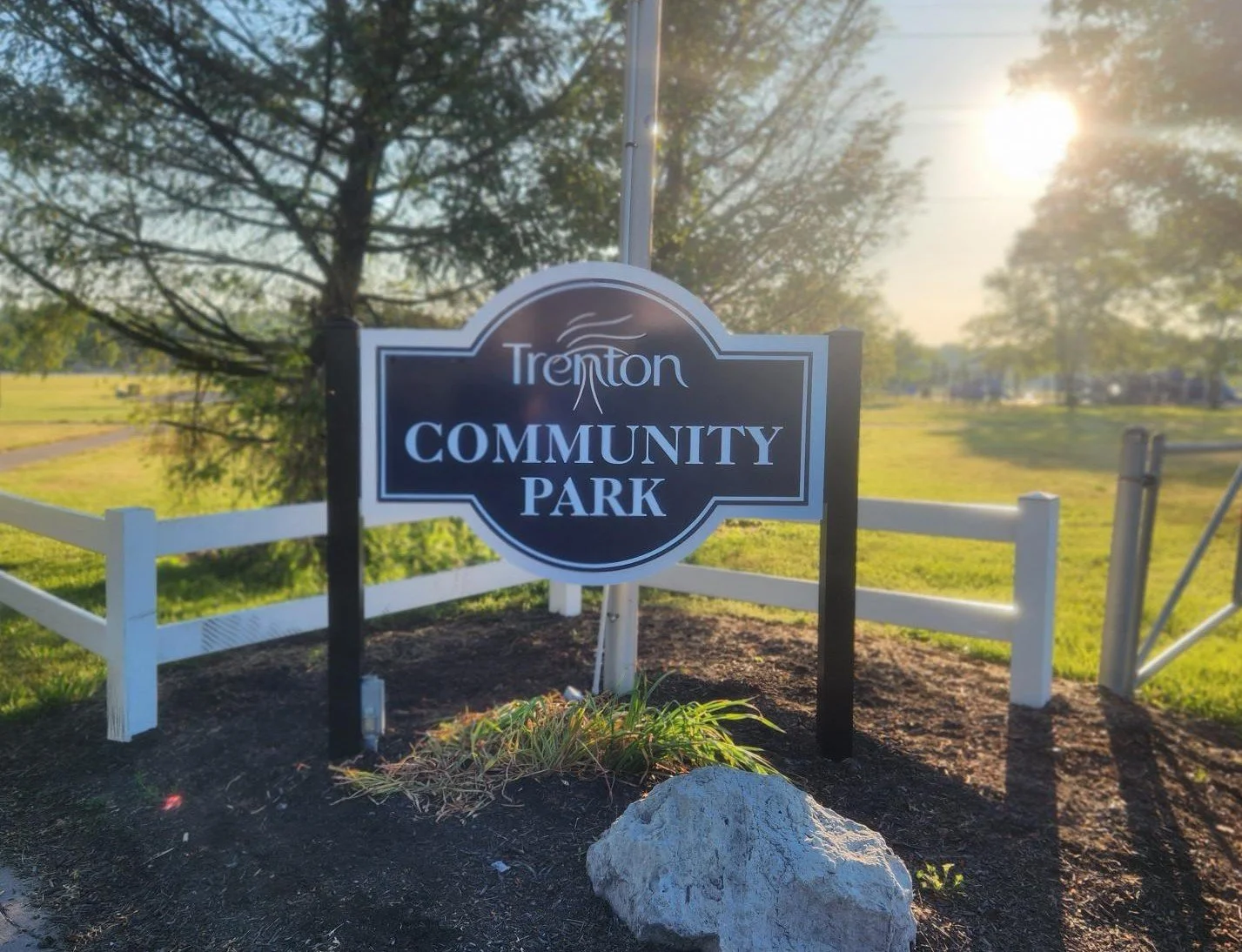 Sign for Trenton Community Park with a tree and grass in the background, sunlight shining through trees.