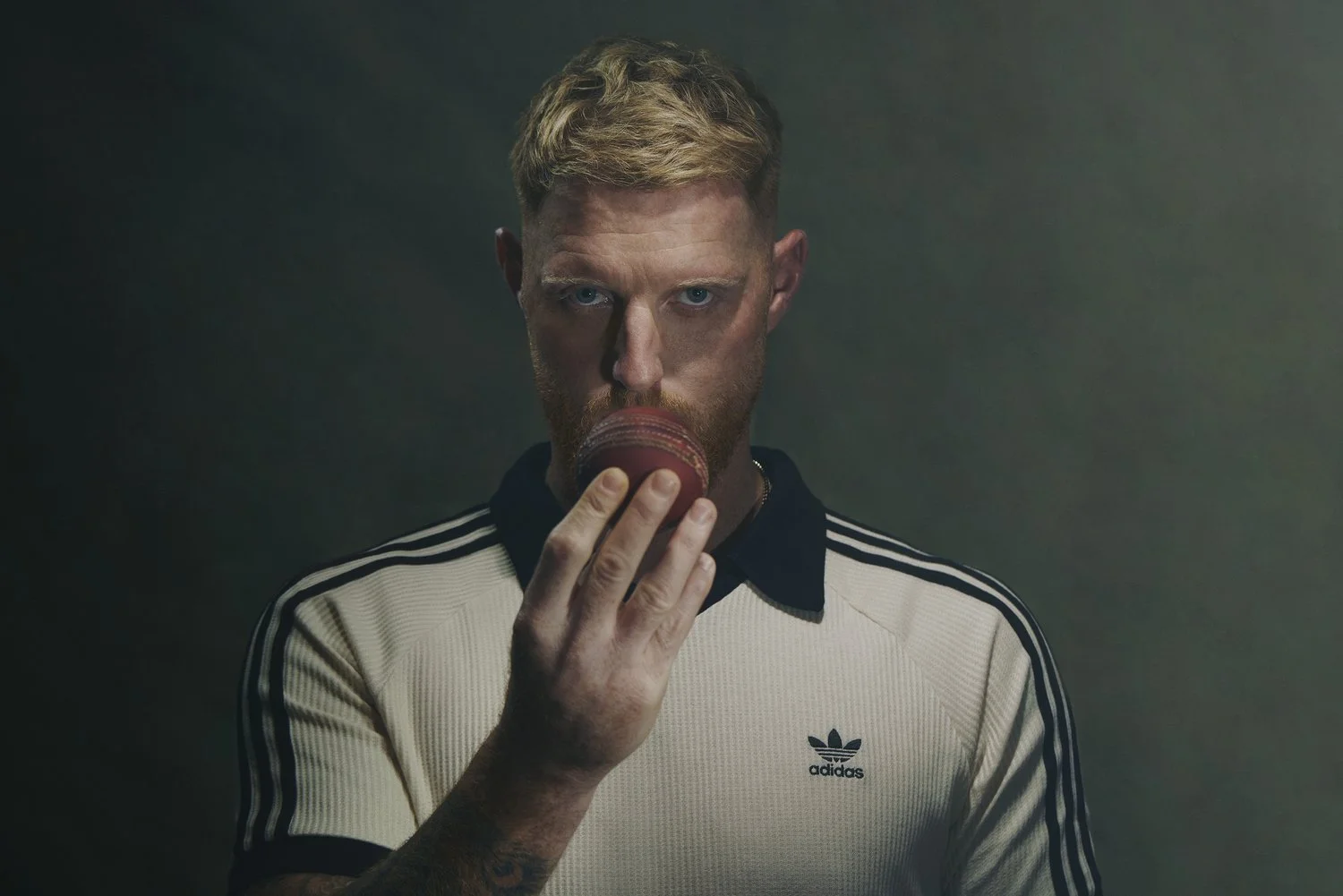 England Cricket Captain Ben Stokes kissing a Cricket Ball, wearing an Adidas sports jersey with black and white stripes.