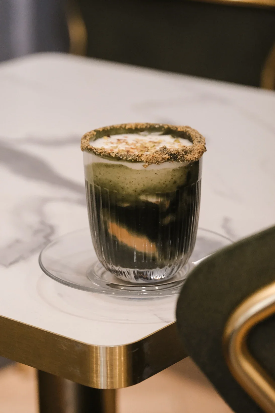 Un verre transparent avec une boisson à plusieurs couches de différentes couleurs, entoure d'un rebord de pâte ou de cookie.