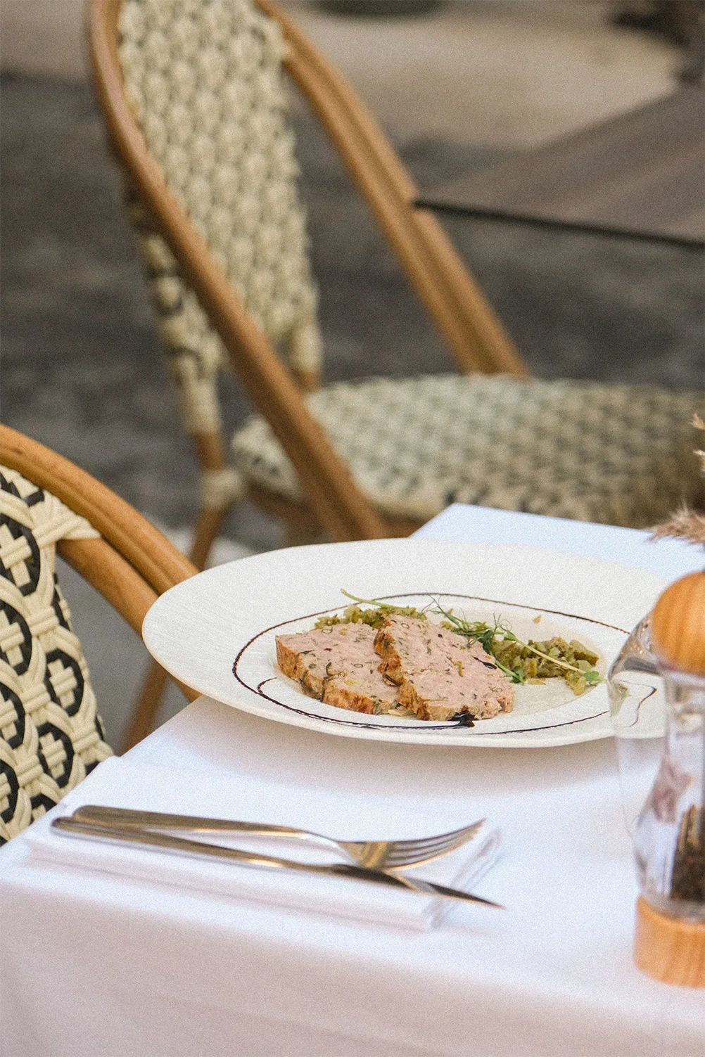 Assiette avec du pâté de campagne et une petite garniture verte, sur une table avec une fourchette et un couteau en aluminium, dans un cadre de restaurant ou banquet.