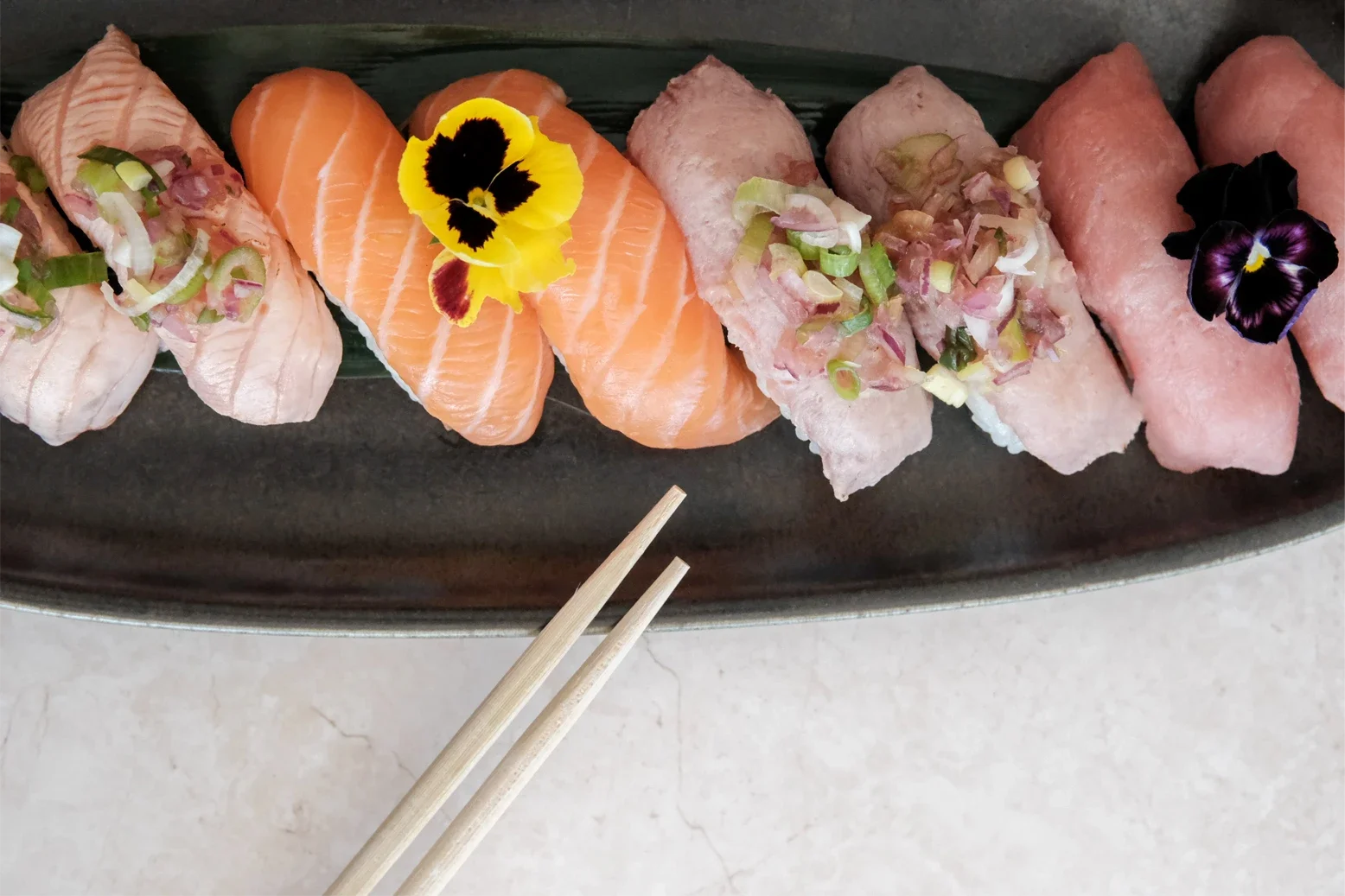 Assortiment de sushis avec des fleurs comestibles sur un plateau noir.