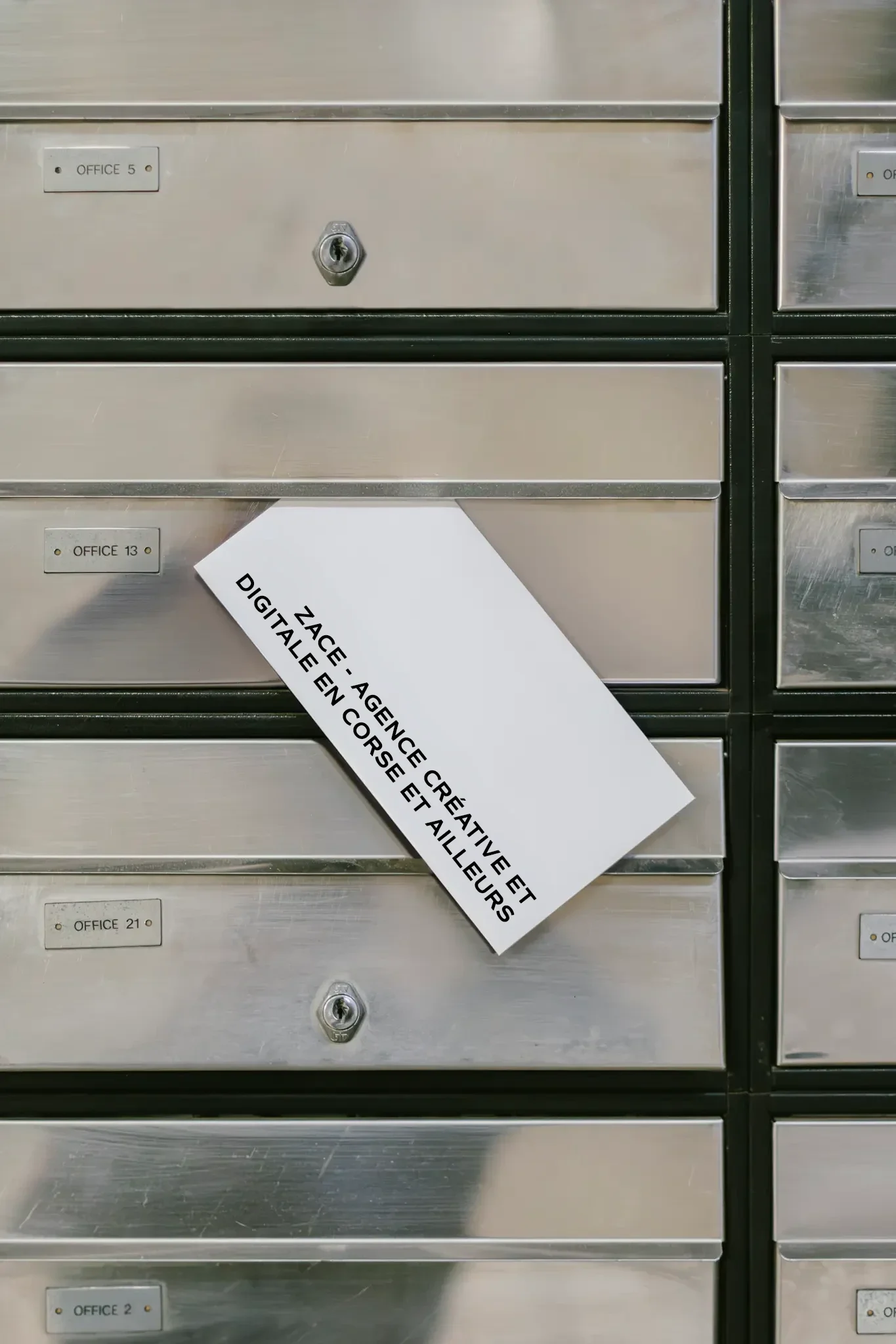 Boîtes aux lettres métalliques dans un immeuble, avec une étiquette blanche déployée indiquant l'adresse de l'agence créative numérique à Couëron.