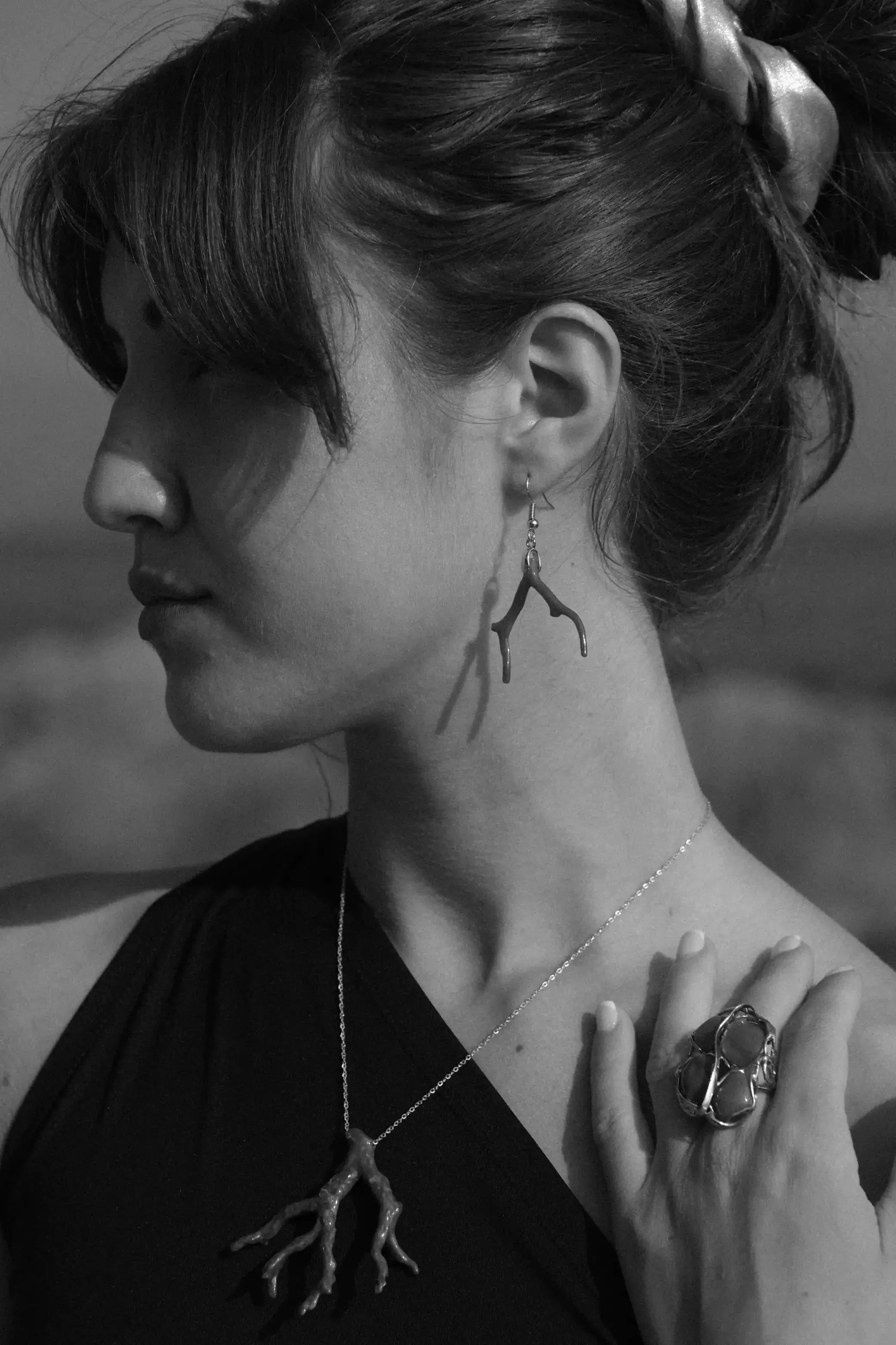 Portrait d'une femme en noir et blanc portant des bijoux, une boucle d'oreille en forme de branche, un collier avec un pendentif, et un bracelet.'}