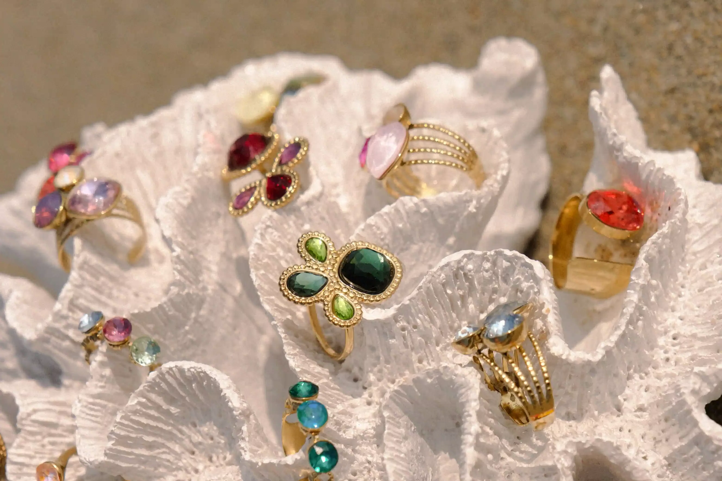 Collection de bijoux en vous avec des pierres colorées, présentée sur un support en forme de coquillage blanc.
