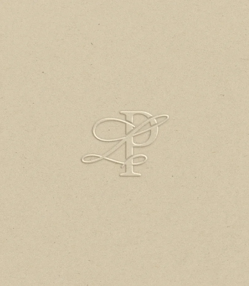 Logo beige avec un monogramme en relief composé d'une lettre D, d'une lettre P et d'une figure de cœur, sur un fond uni