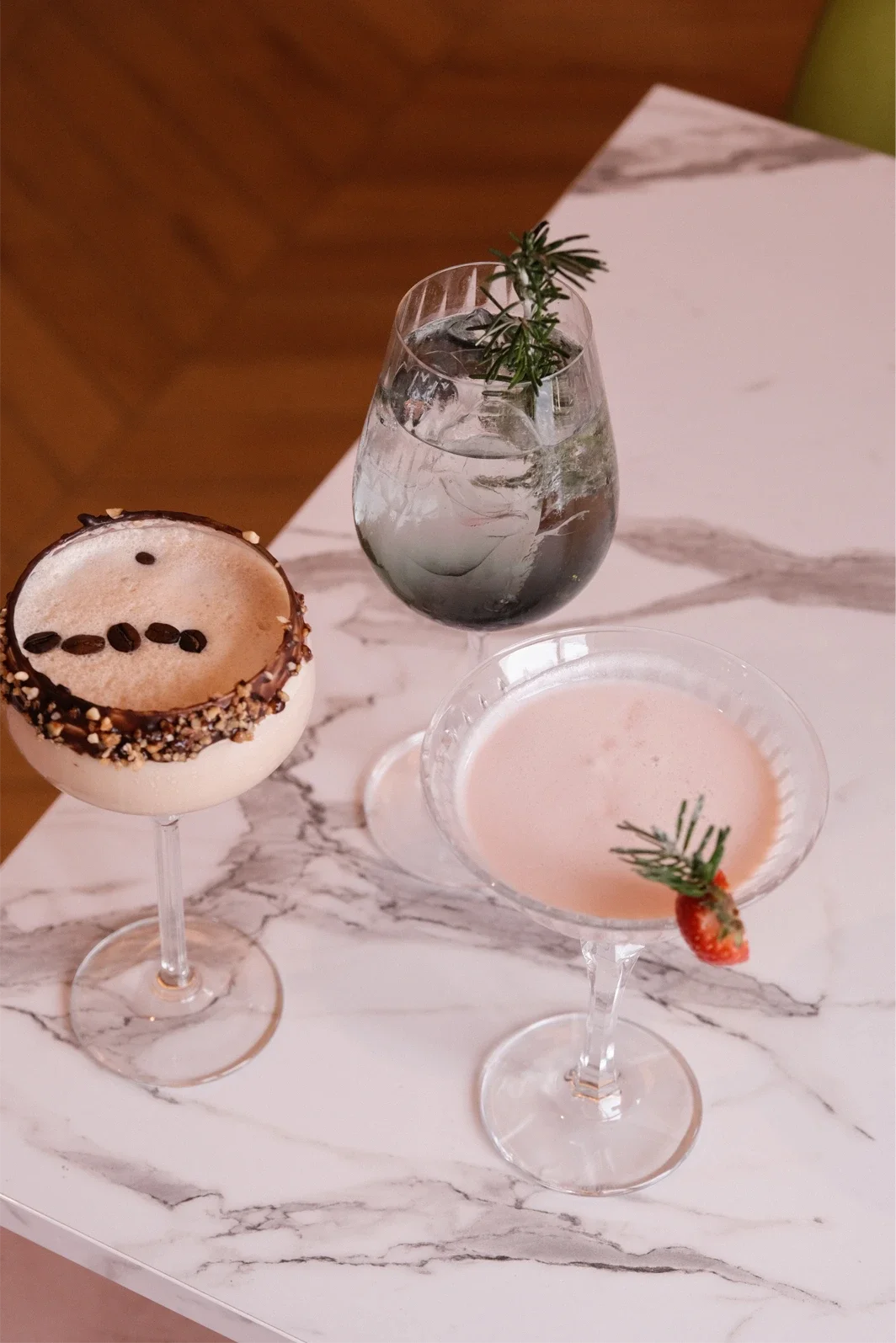 Trois cocktails sophistiqués avec décoration de romarin et fraise sur une surface en marbre.