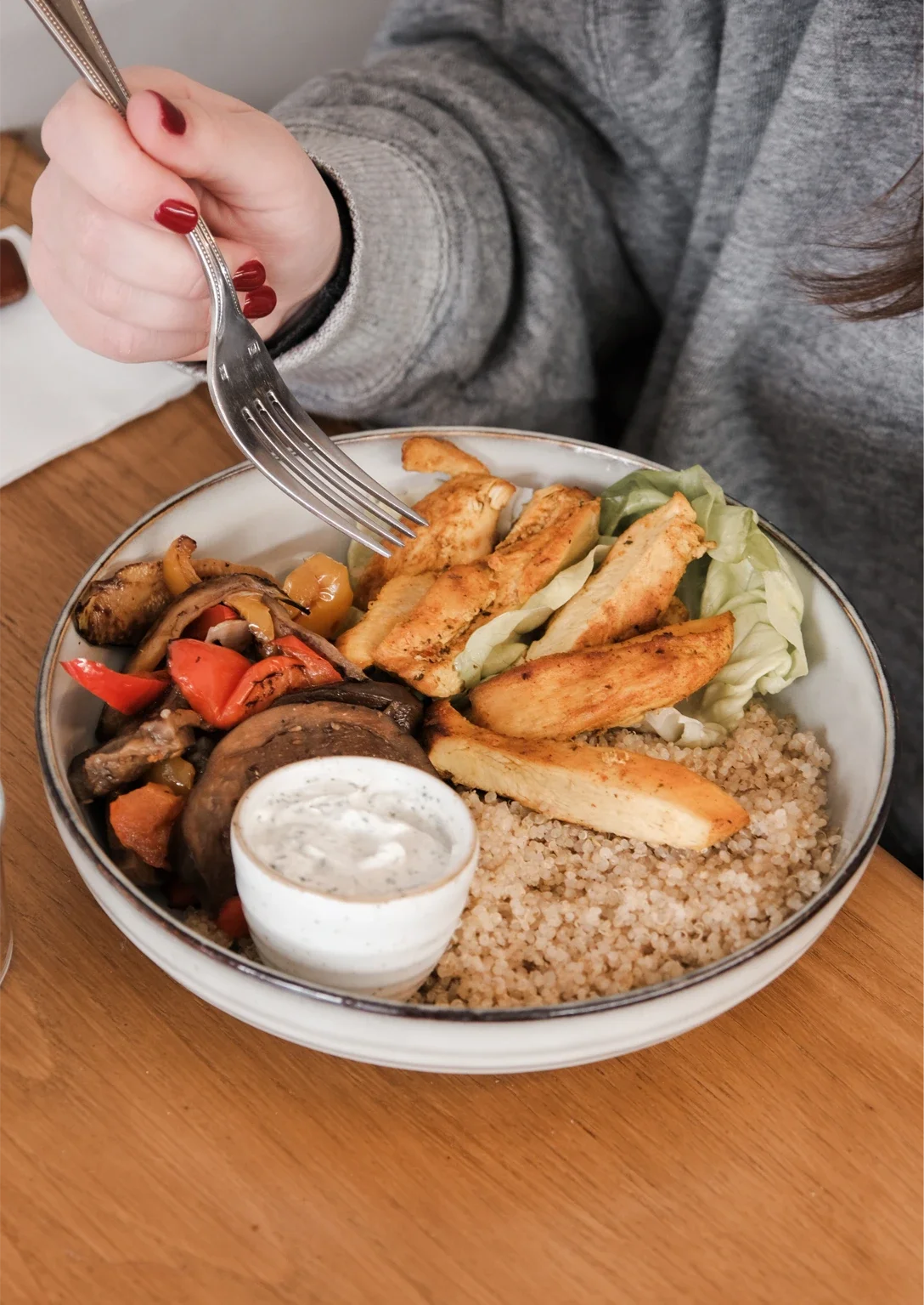 Assiette de nourriture végétarienne avec du couscous, des légumes rôtis, du tofu grillé, une sauce au yaourt, et des pommes de terre frites, sur une table en bois.