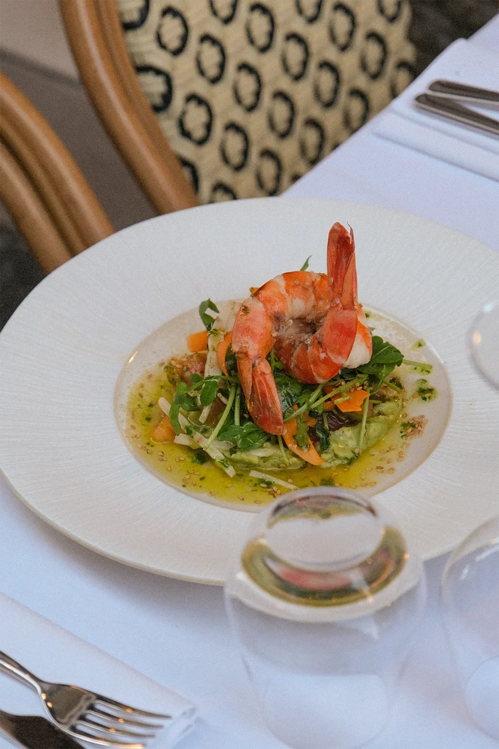 Salade avec crevettes rouges, légumes verts et vinaigrette, présentée dans une assiette blanche à bords larges.
