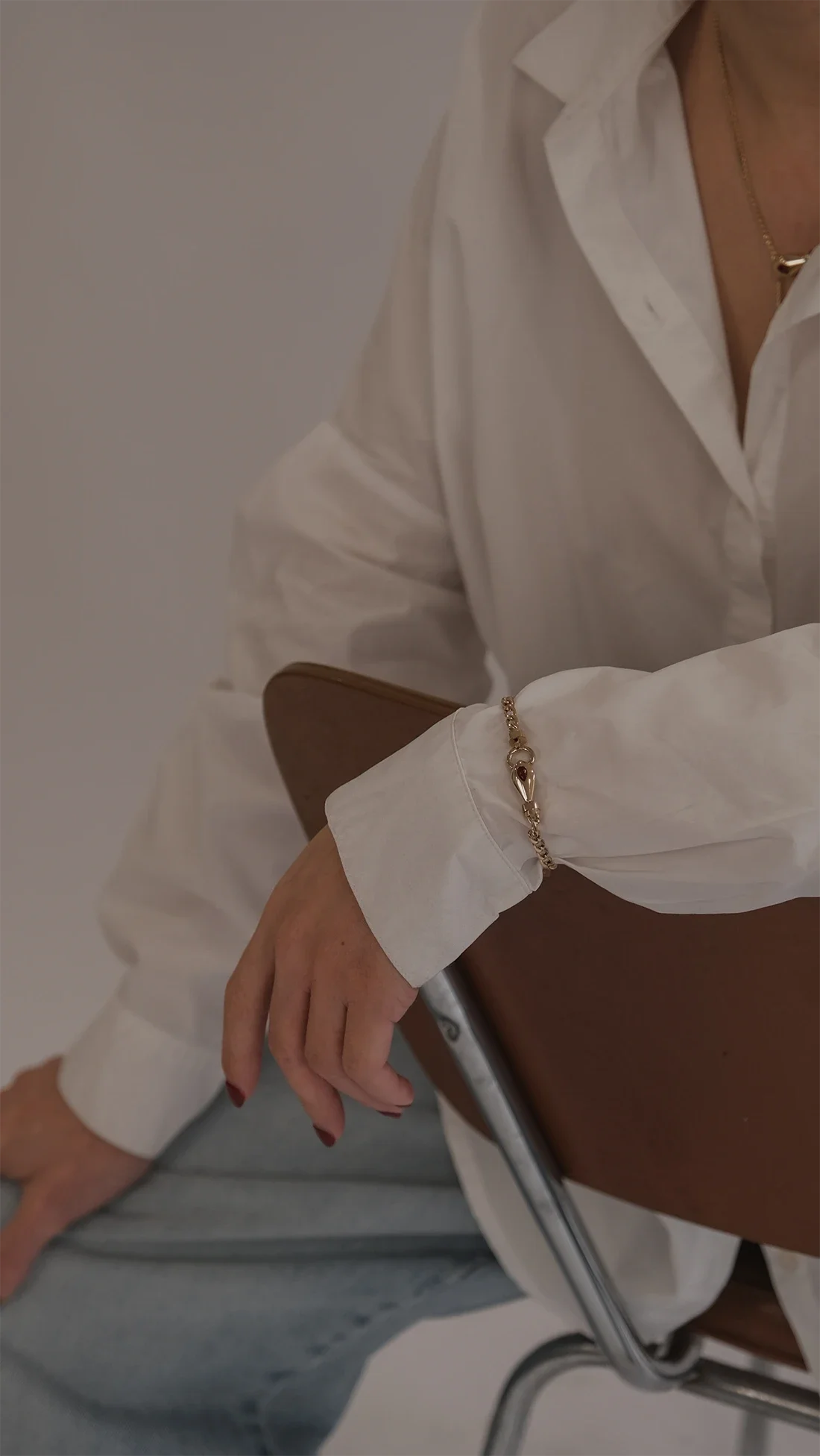 Main portant une bracelet en or avec un motif de tête de manchette et une robe en blouse blanche, assise sur une chaise en métal.