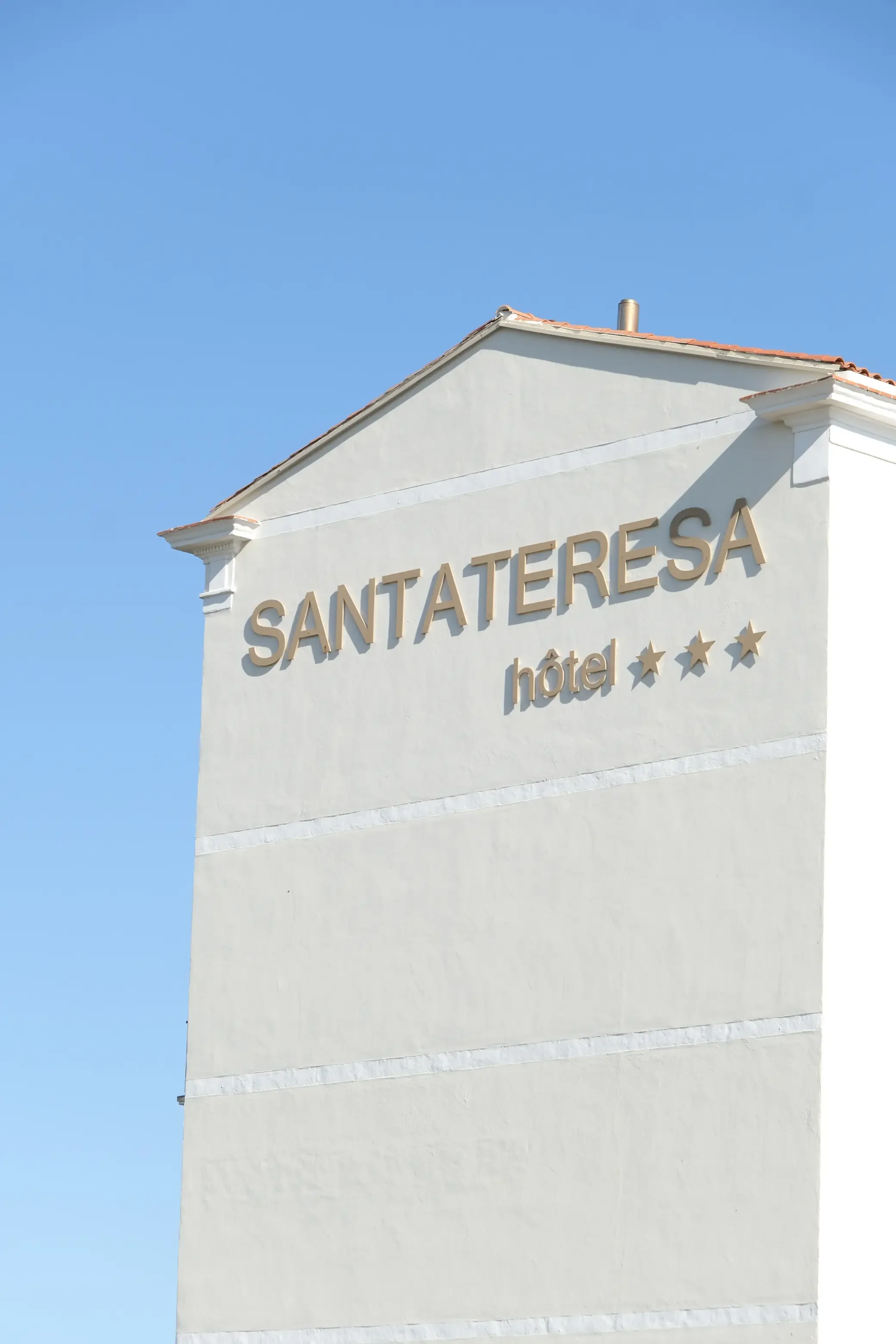 Façade d'un hôtel appelé SANTATERESA avec des étoiles indiquant un classement de trois étoiles, contre un ciel bleu clair.