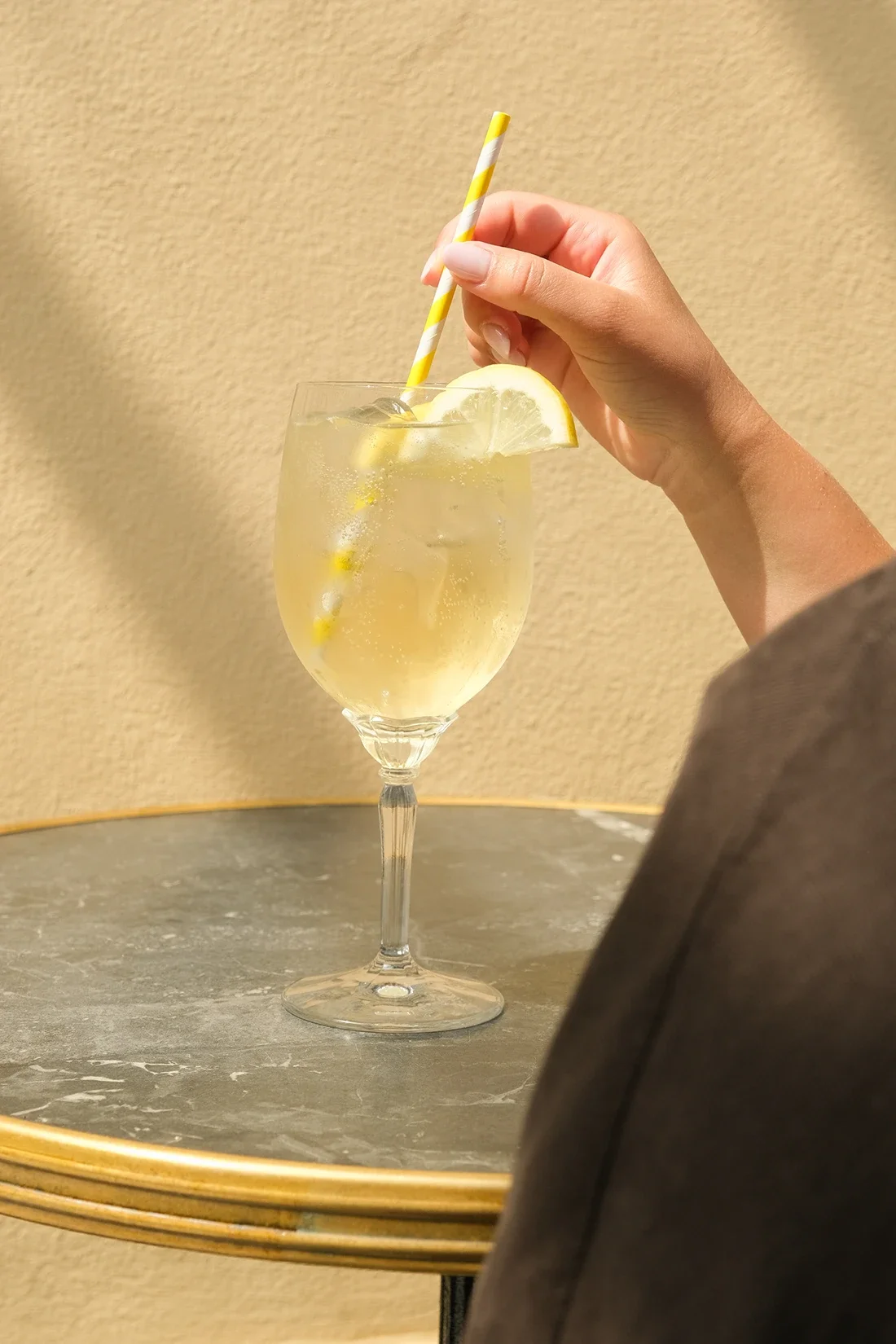 Verre à cocktail avec tranche de citron, boisson jaune pétillante, avec paille rayée jaune et blanc, posé sur une table ronde en marbre