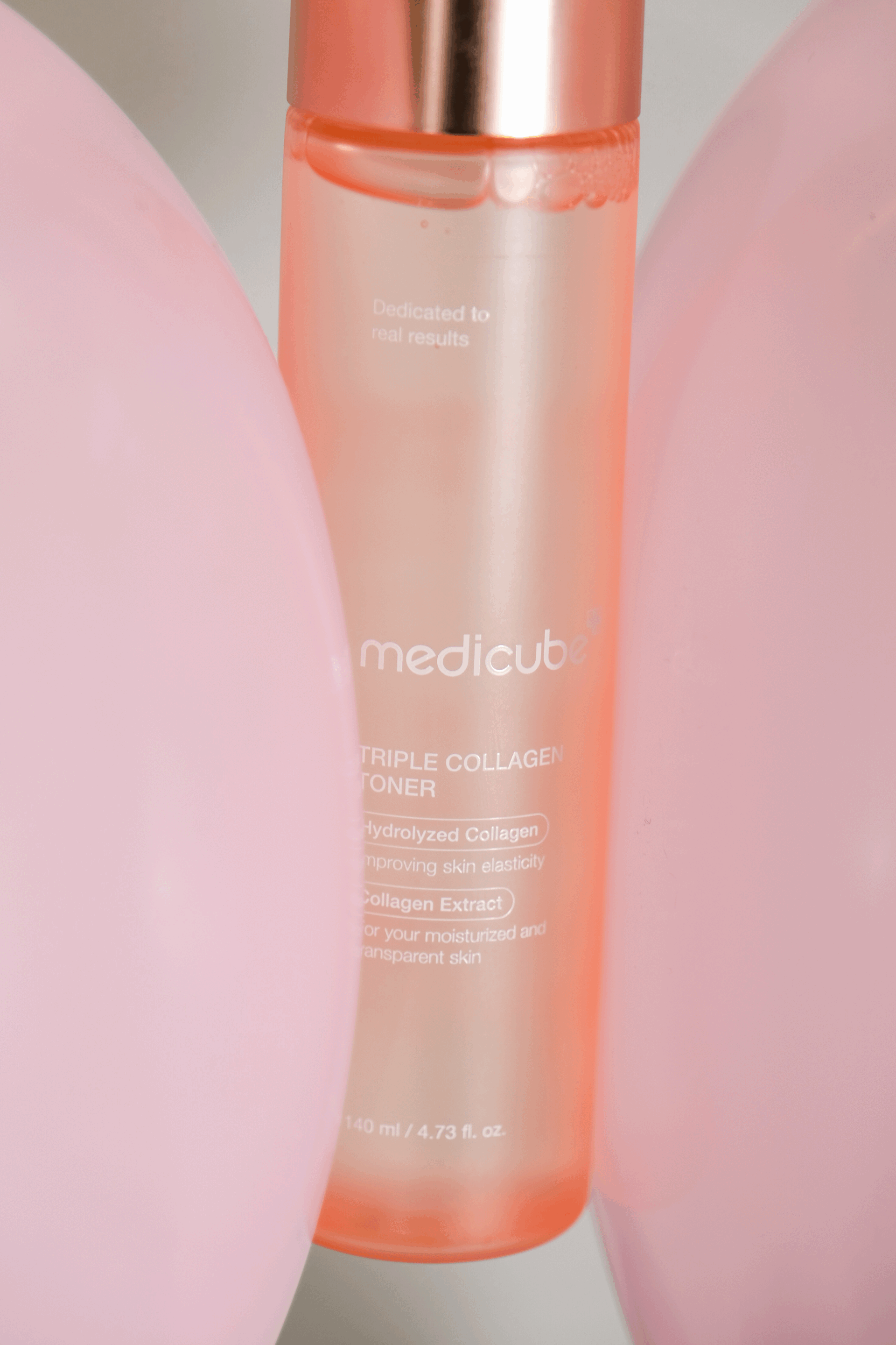 Flacon de toner rose avec texte blanc, portant la marque 'medicube' et descriptions de produit, entouré de deux objets roses.