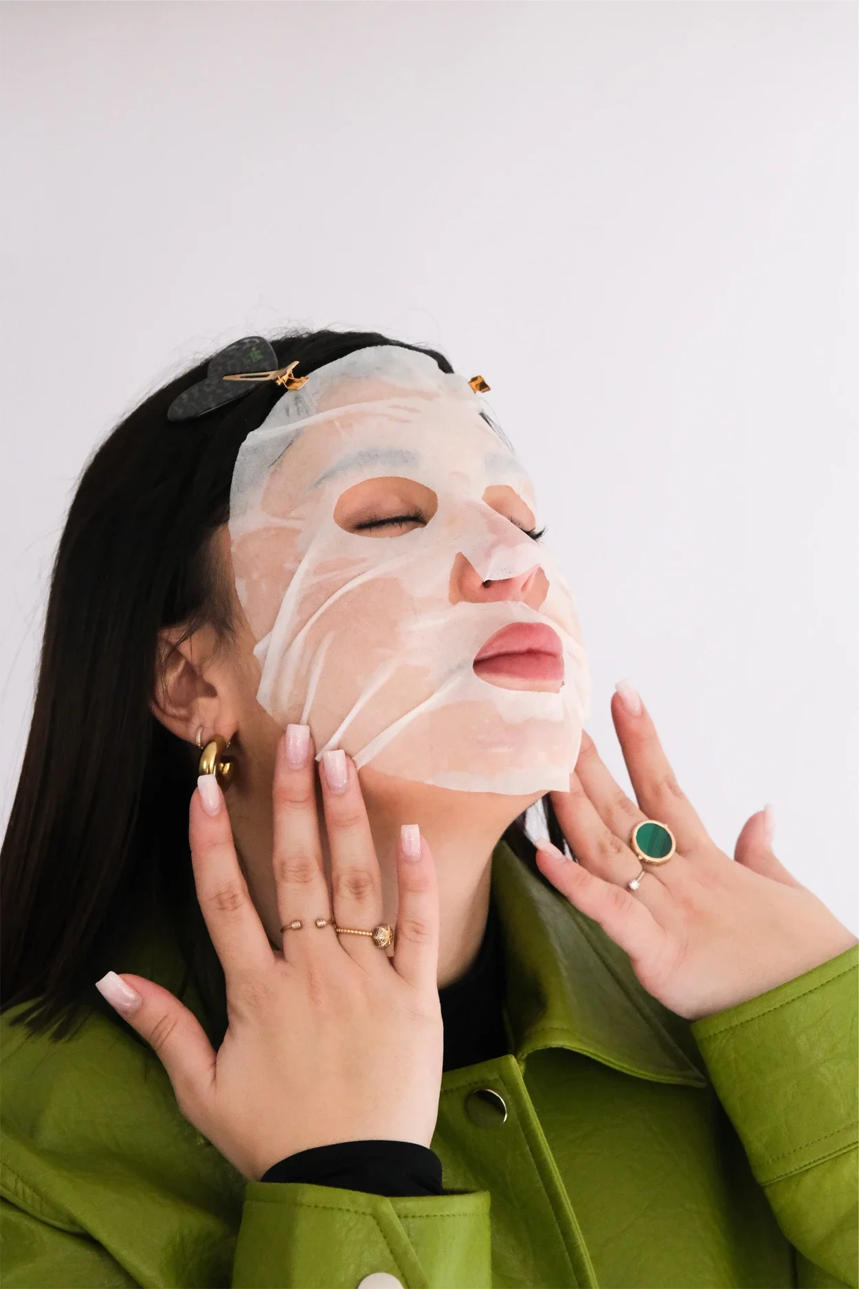 Une femme portant un masque facial en train d'appliquer un soin, avec plusieurs mains qui la touchent, dans un contexte de soin de la peau.
