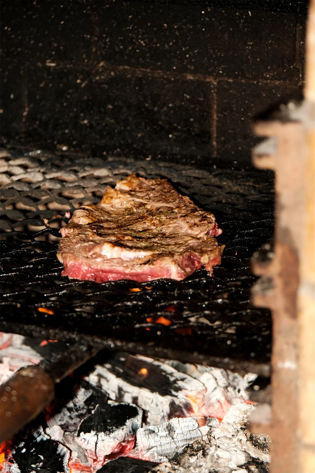 Une tranche de viande en train de cuire sur un grill à braises avec un fond sombre.