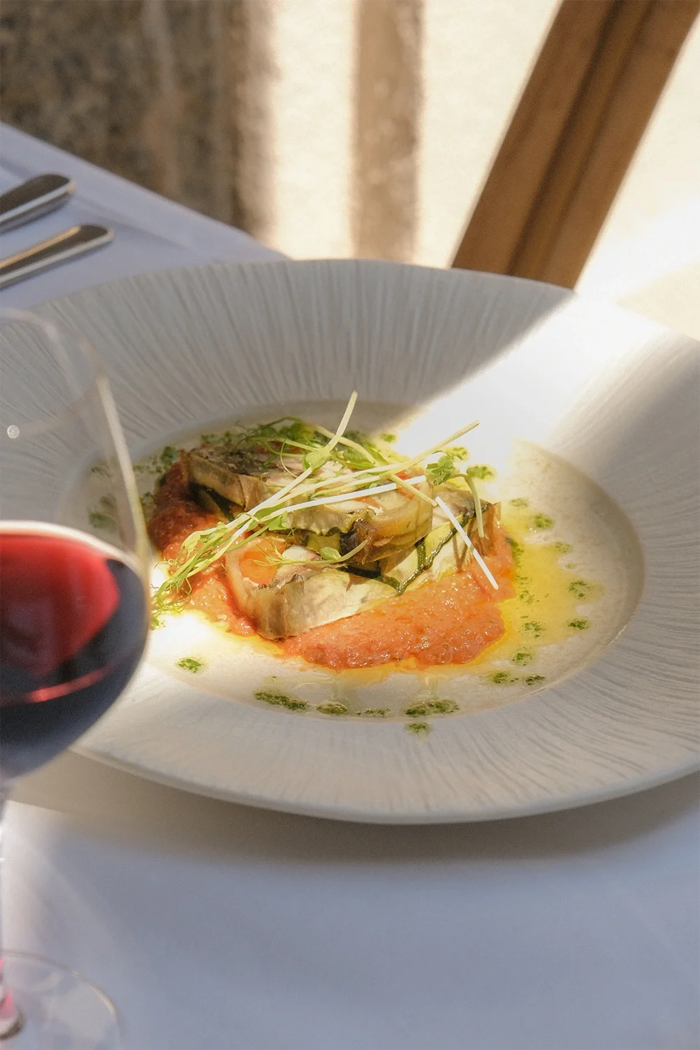 Un plat gourmet avec des légumes et une sauce dans un bol blanc, accompagné d'un verre de vin rouge.