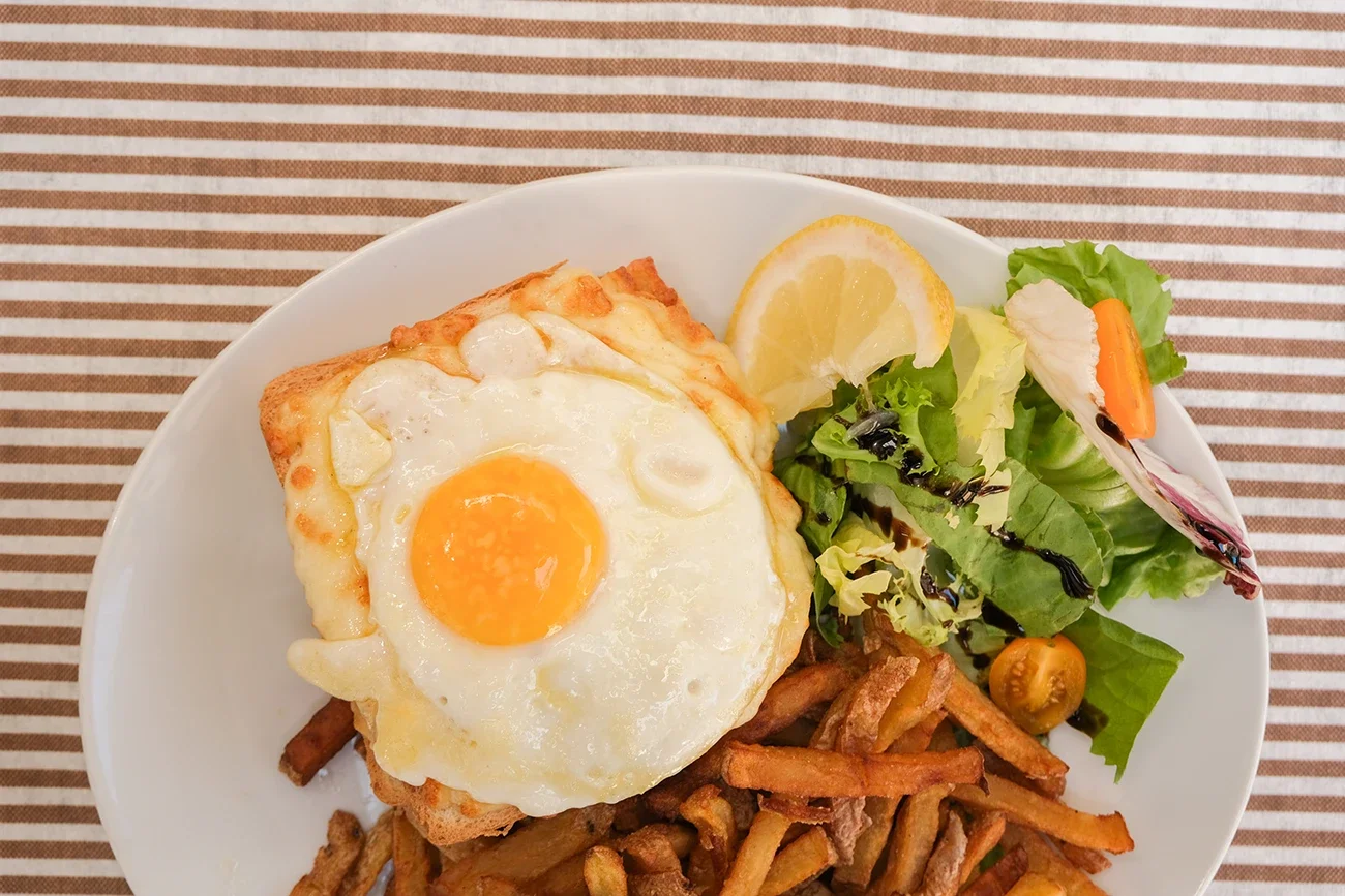 Assiette contenant un œuf au plat, des frites, une petite salade avec une tranche de citron, des tomates cerises, et une vinaigrette