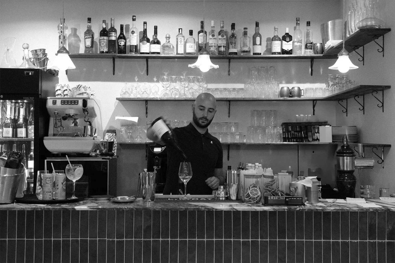 Un bartender verse du vin dans un verre derrière un comptoir de bar avec étagères de bouteilles d'alcool en arrière-plan.