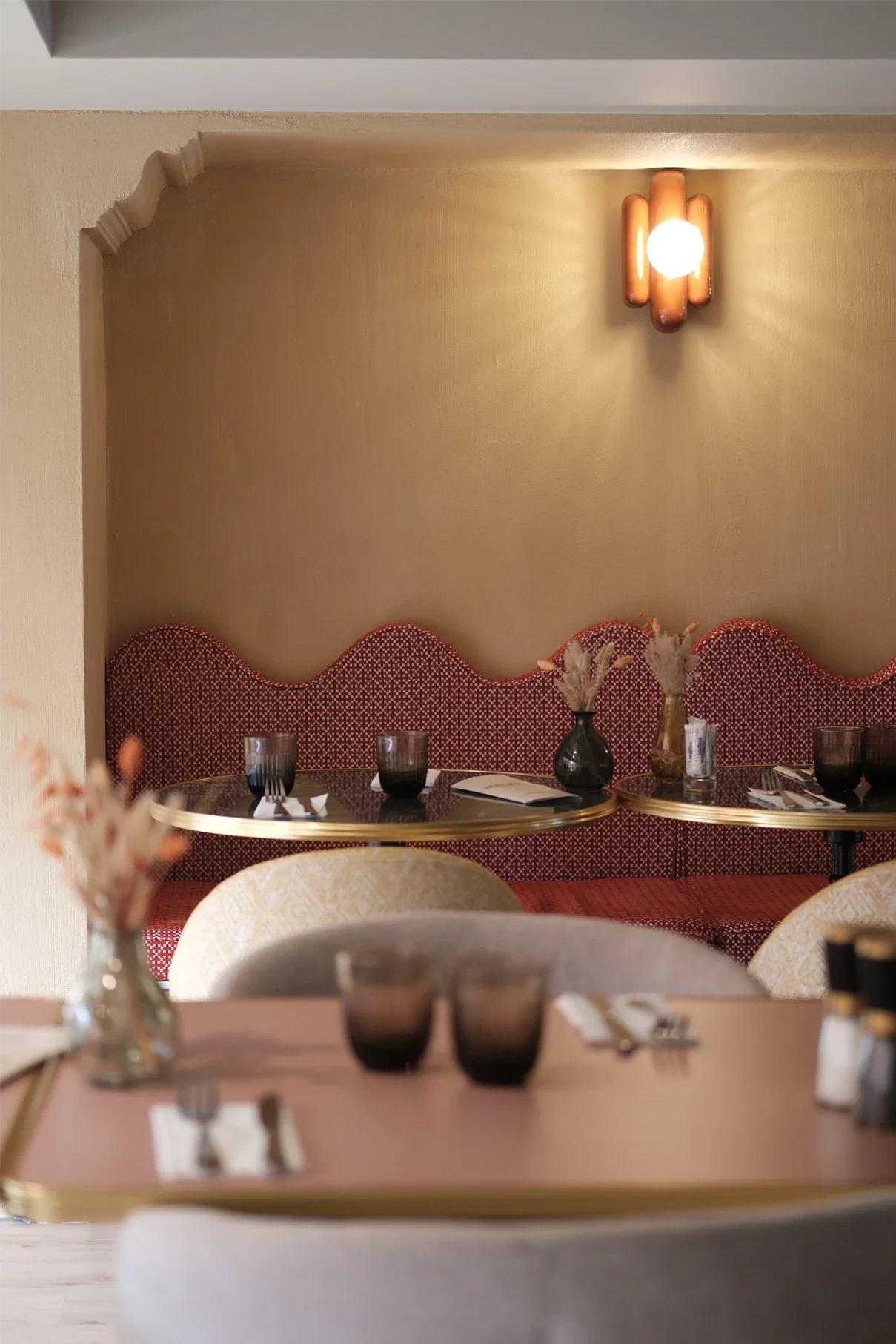 Intérieur d'un restaurant avec une table dressée, verres, assiettes, et un décor élégant avec des vases et un éclairage chaleureux.