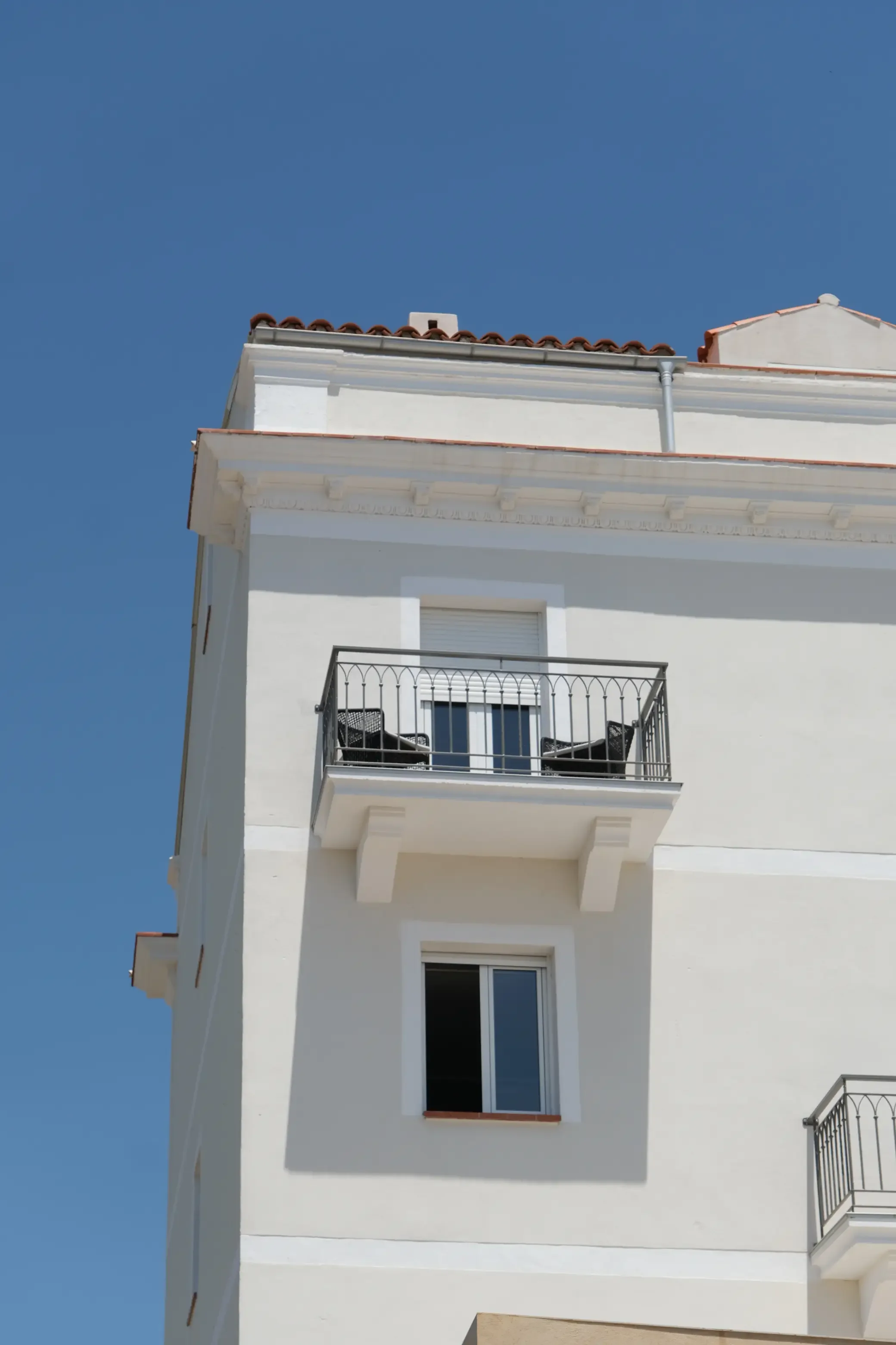 Vue d'un bâtiment blanc avec des balcons en fer forgé sous un ciel clair.