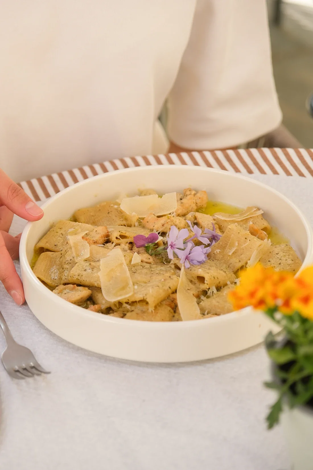 Plat de pâtes fraîches garnies de parmesan, de fleurs comestibles et de feuilles d'herbes, présenté dans un bol blanc.