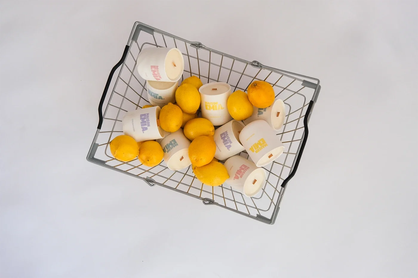 Panier de rangement en métal contenant des citrons et des bougies dans des supports en carton blanc avec des inscriptions colorées.