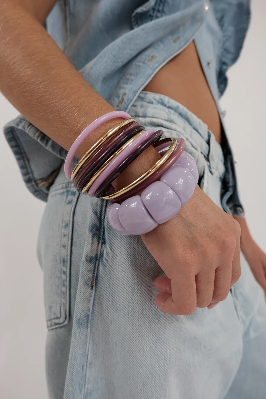 Poignée de plusieurs bracelets colorés en pastel, en train d'être portée par une personne portant un jean décontracté.
