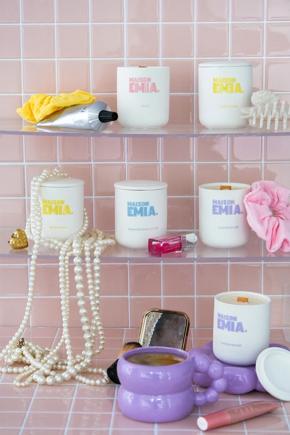 Étagère avec des bougies, des bijoux, des produits de beauté, un miroir, et divers accessoires dans une salle de bain au décor rose.