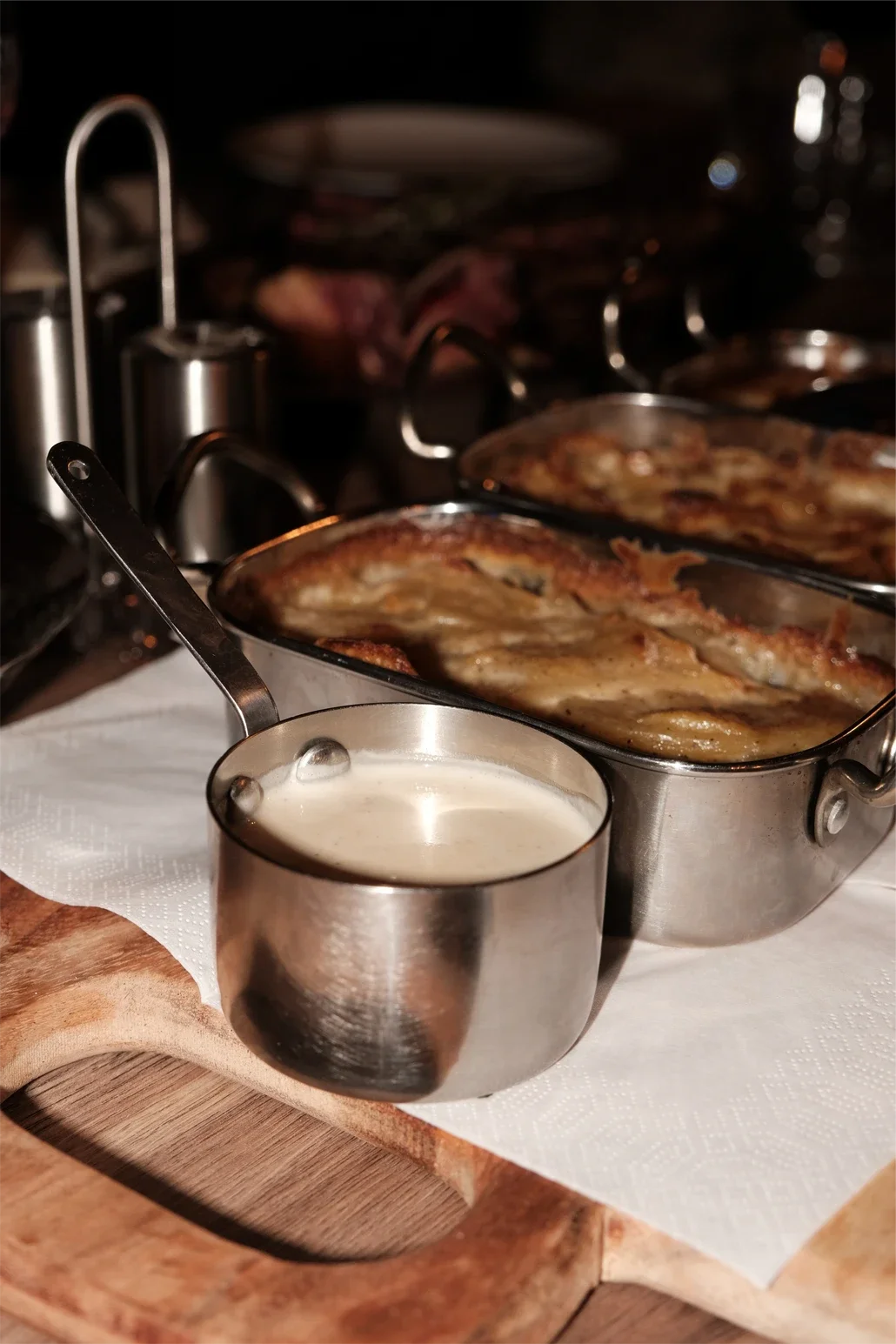 Plat de poisson cuit avec une sauce blanche, servi dans une casserole en métal, sur une planche en bois, avec une nappe blanche.